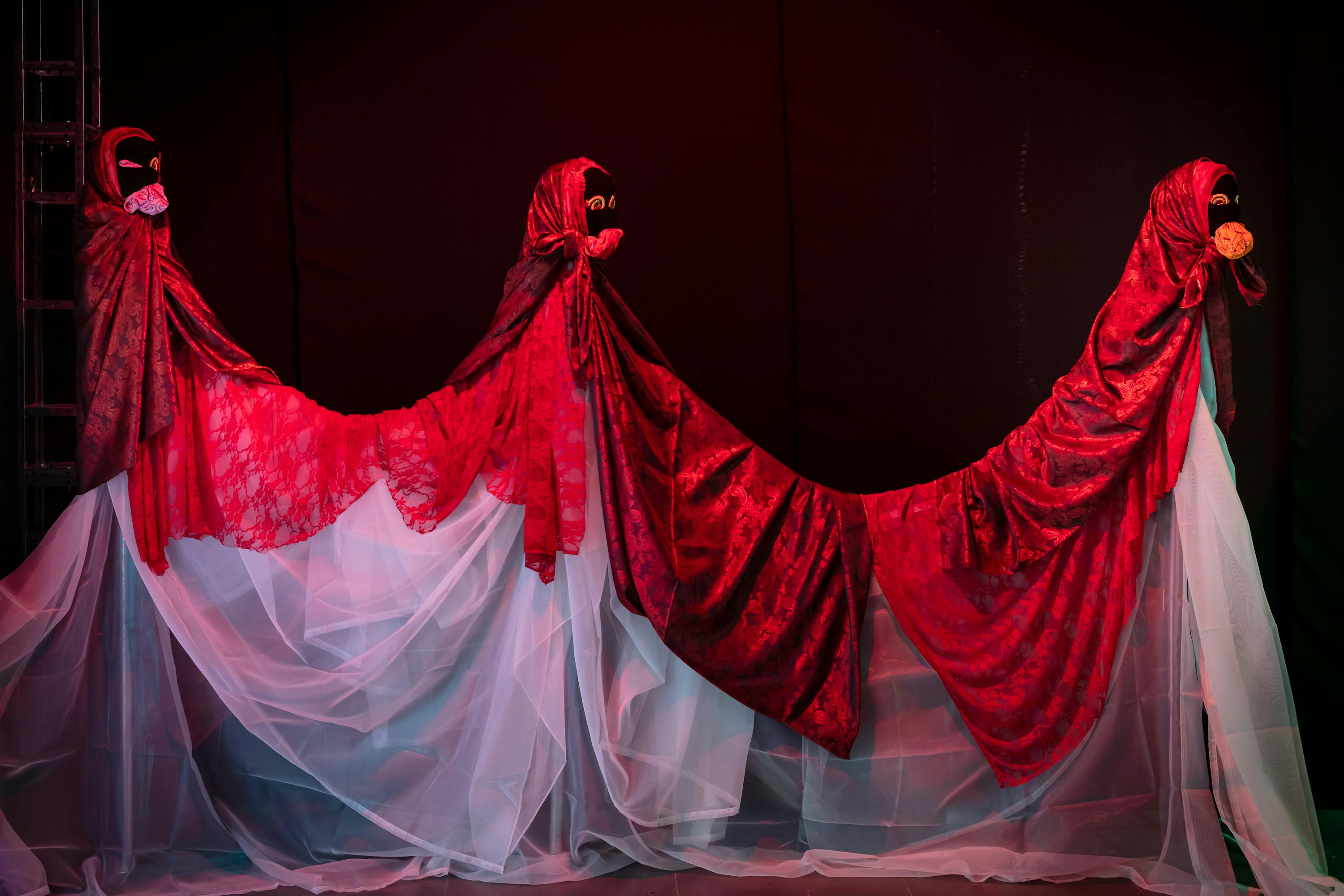 A sculpture comprising three mannequins connected by white draped chiffon and red velvet fabric