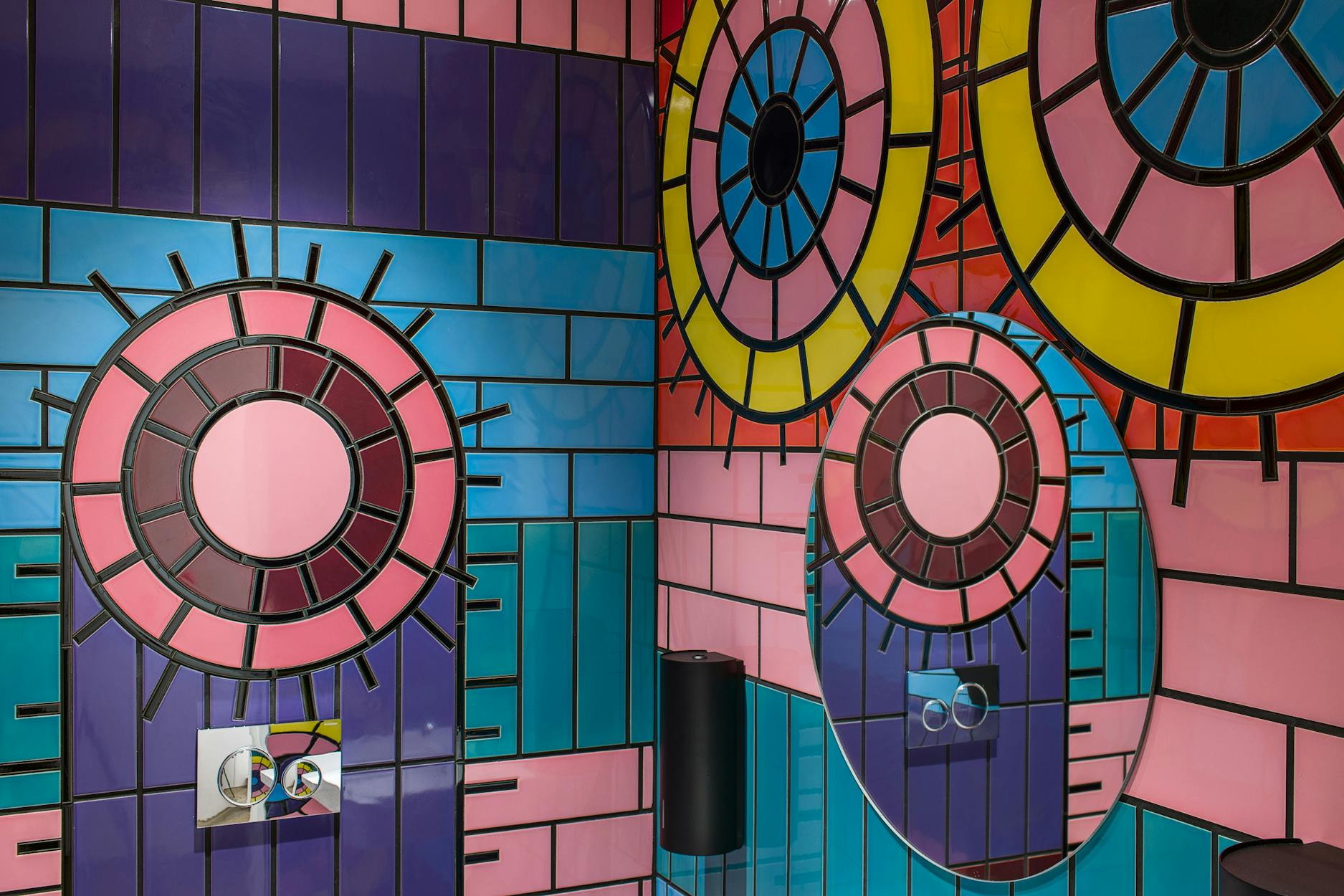 Colorful geometric wall art featuring concentric circles in red, yellow, orange, and pink, outlined with black lines, alongside blue rectangular shapes and a round, black protruding object.