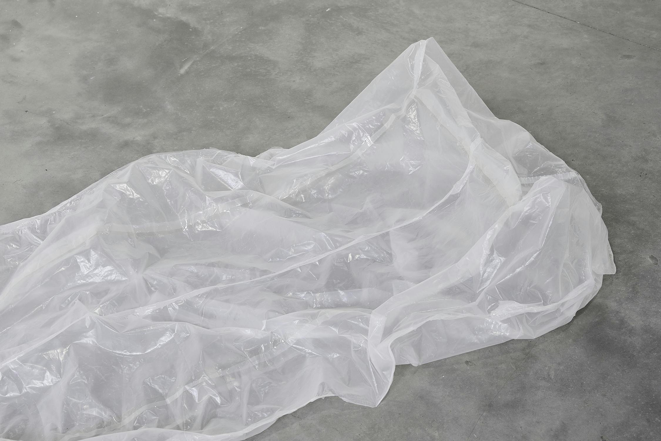 A crumpled, transparent plastic sheet lies on a smooth, grey concrete floor.