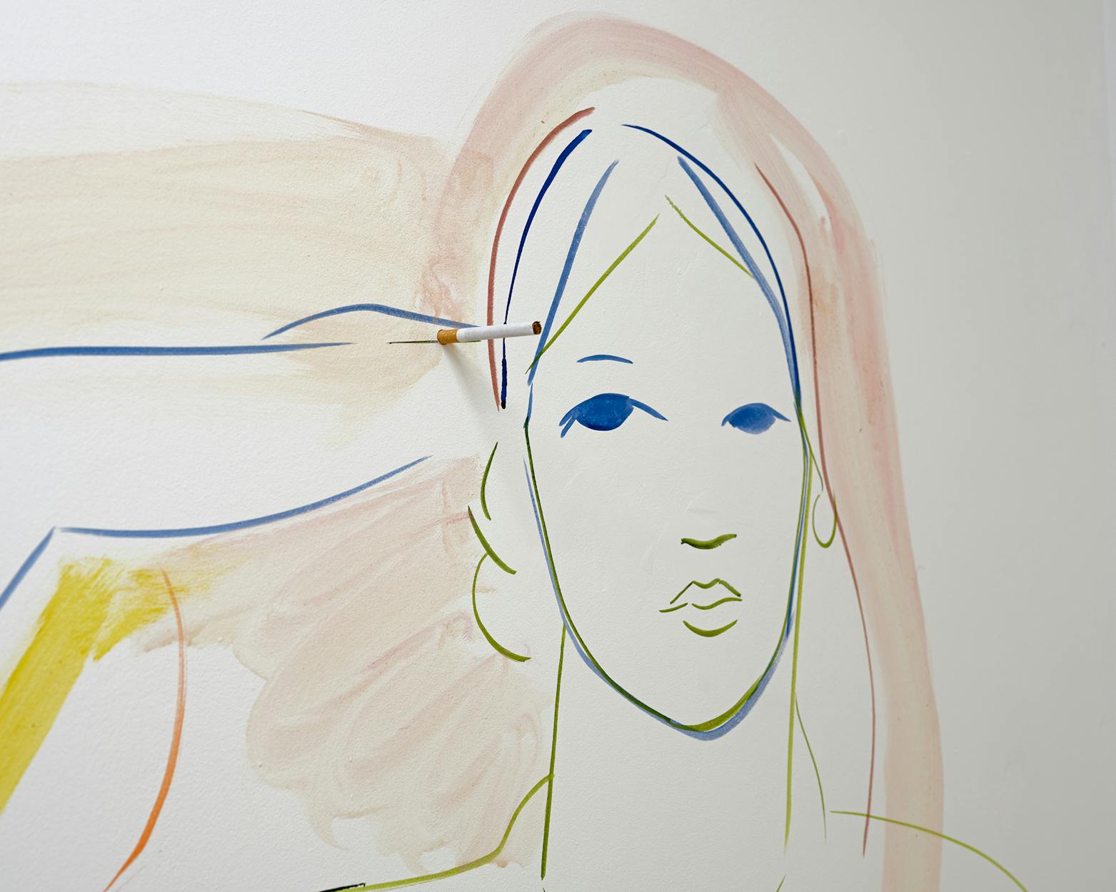 A minimalistic artwork of a woman’s face in pastel colours is painted on a wall. A hand, also painted, inserts a real cigarette behind her ear, blending the physical object with the illustration.