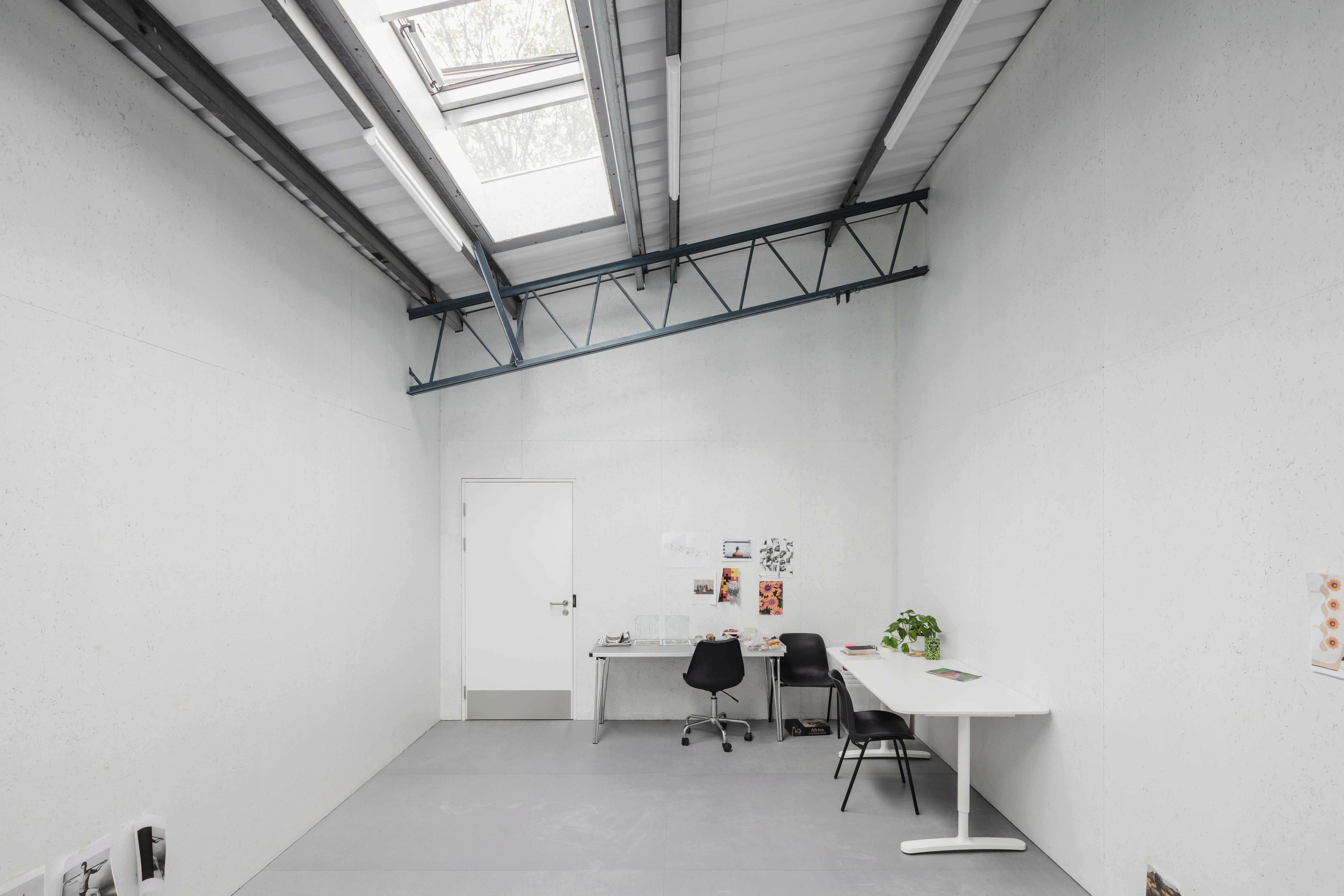 an artist's studio with white walls, slanted roof and exposed steal beams. The roof has a skylight window.