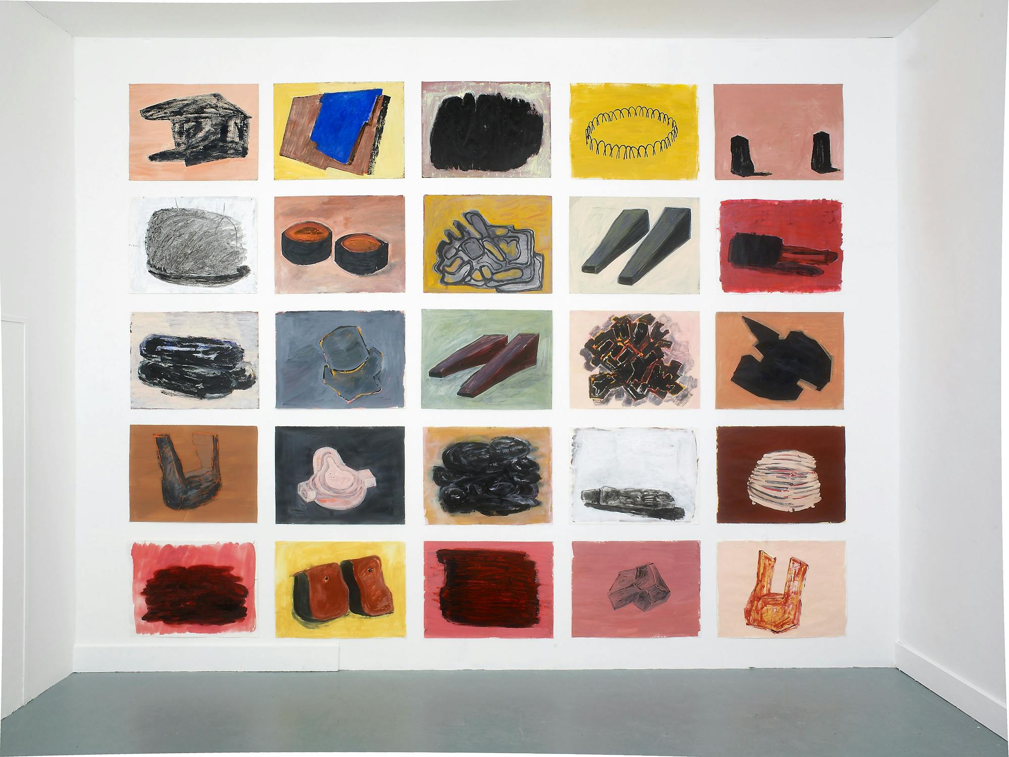 A white wall displays a 5x5 grid of abstract paintings. Each square features objects or shapes in muted colours—mostly reds, pinks, browns, and greys—depicting items like shoes, books, bowls, gloves, and geometric forms on coloured backgrounds.