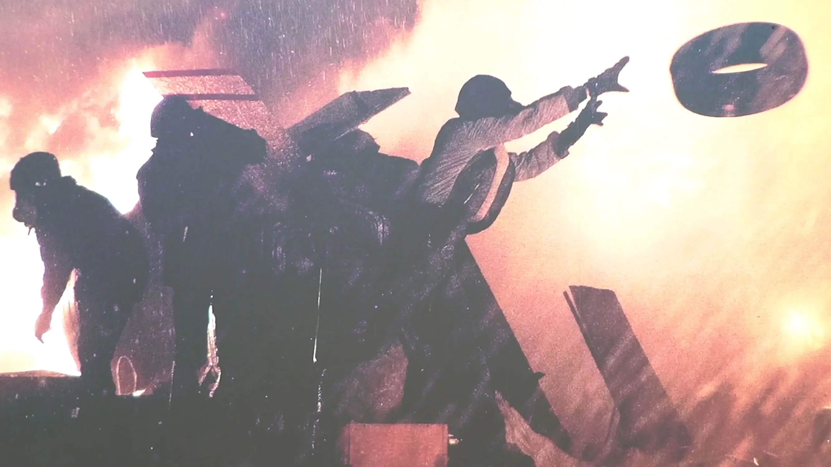 Silhouetted firemen work near a large, glowing fire. One fireman in the foreground reaches out towards a flying disc-shaped object in the air.