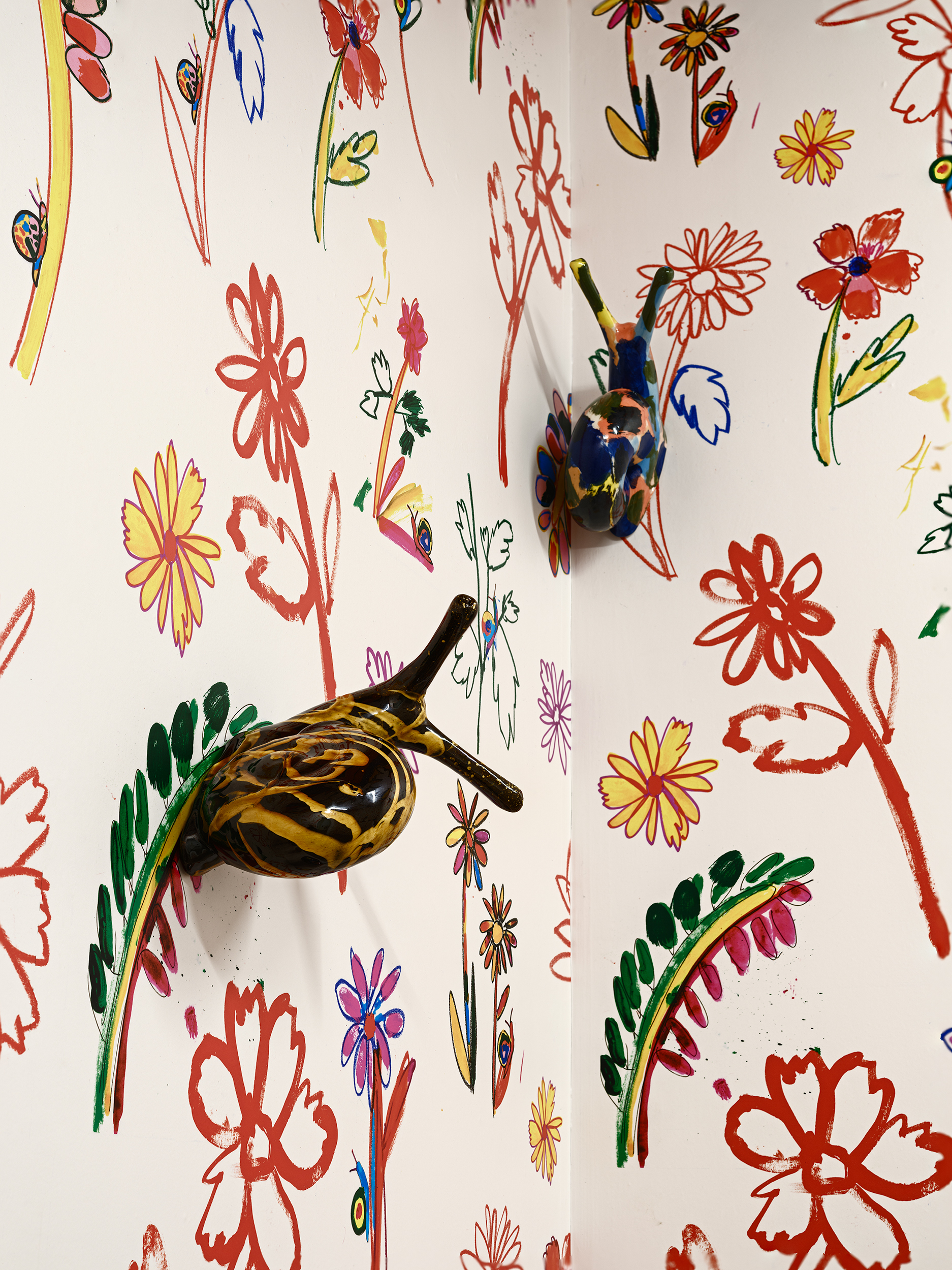 Colourful, whimsical glazed ceramic snails attached to a corner wall covered in vibrant, hand-drawn flower patterns in red, yellow, pink, and green.