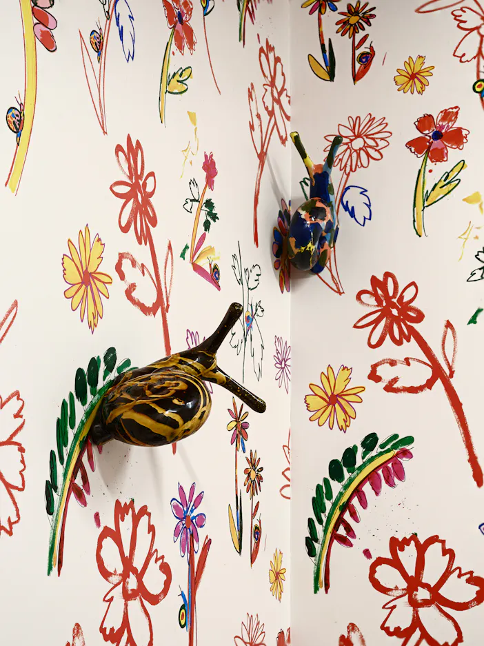 Colourful, whimsical glazed ceramic snails attached to a corner wall covered in vibrant, hand-drawn flower patterns in red, yellow, pink, and green.
