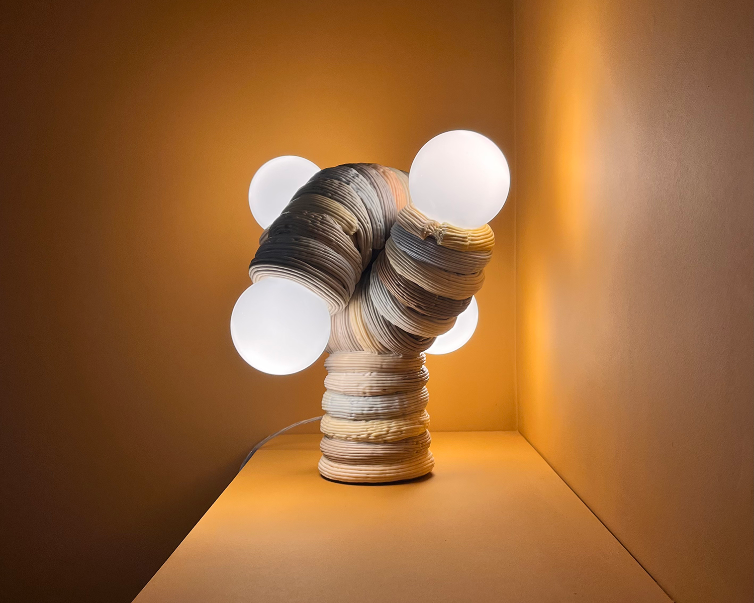 A sculptural table lamp with a curved created by James Shaw, with a ribbed plastic body in neutral tones, featuring four round white bulbs extending outward, is displayed on a yellow shelf against a matching yellow background.