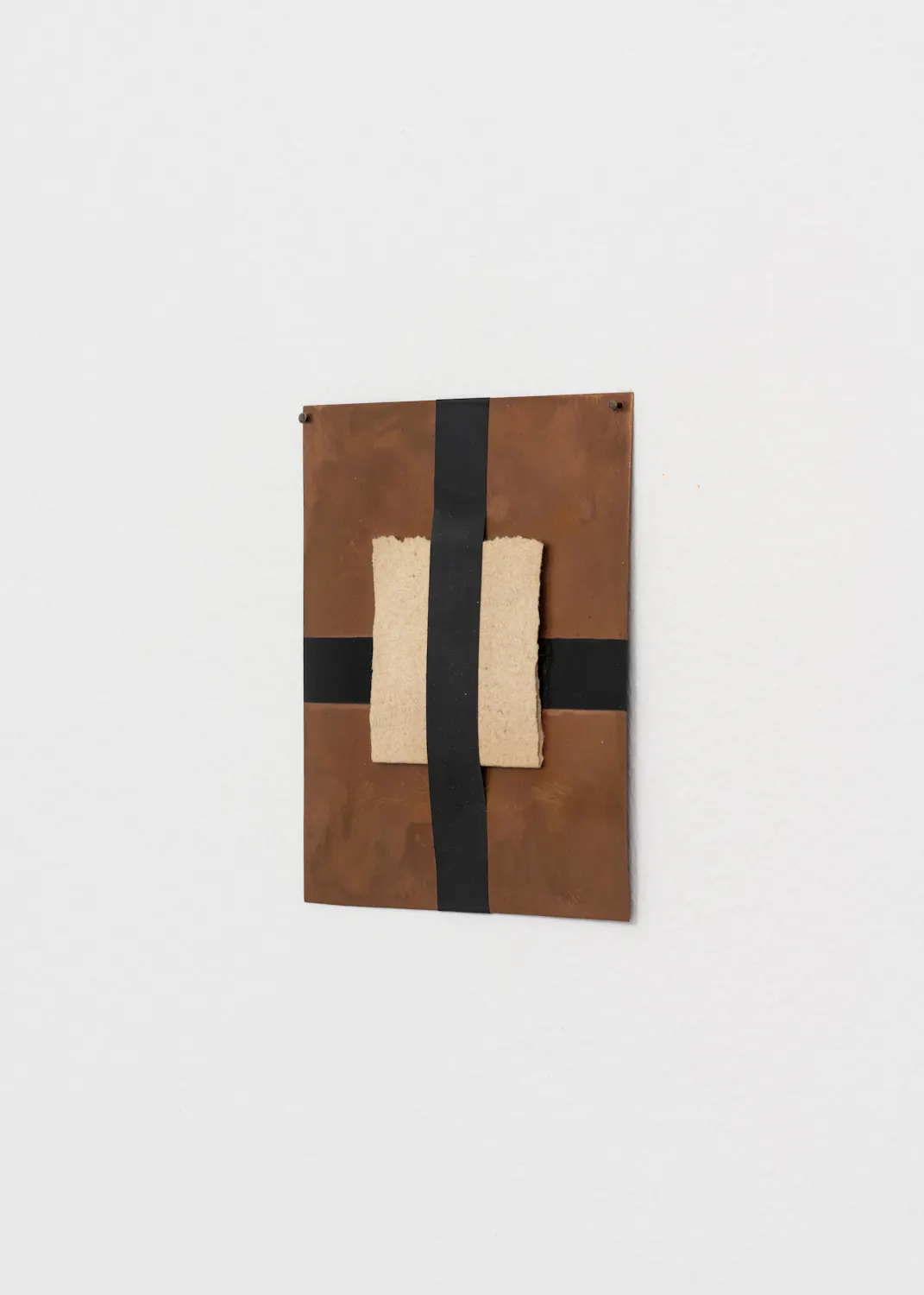 A small, multi-layered sculpture mounted on a plain white wall. The piece features a rough, dark brown copper base topped with a band of teal paint, a smooth black angled ledge, and a jagged, rusty metal top edge.