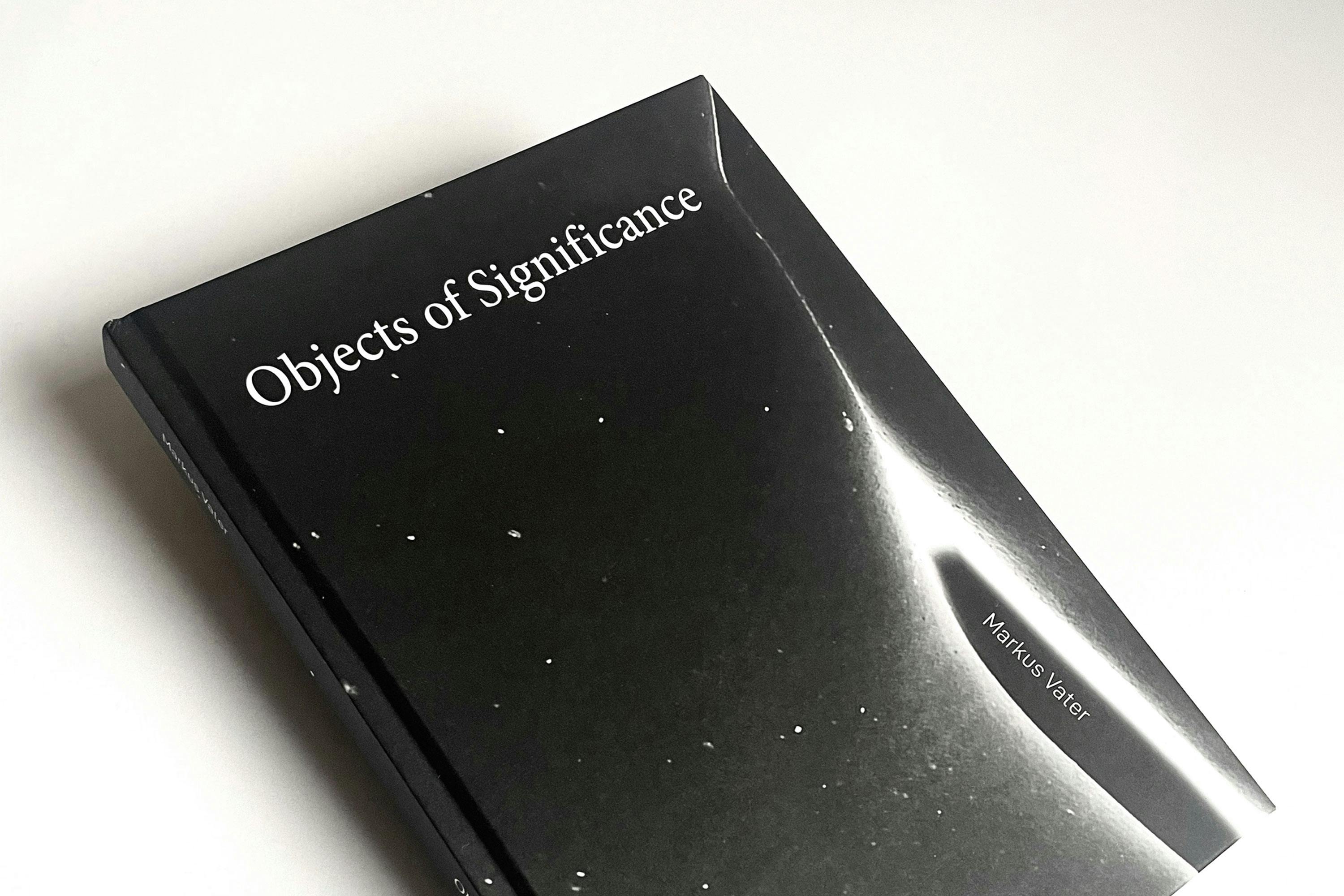 A black hardcover book titled "Objects of Significance" by Markus Vater lies on a white surface. The cover features a minimalistic design with small white specks scattered across it.