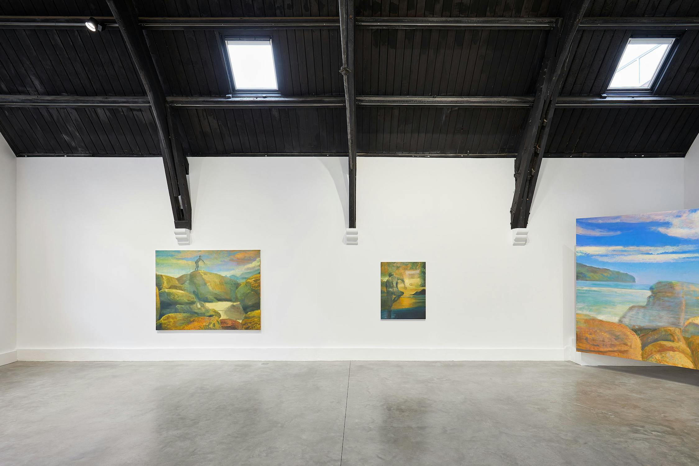 A modern art gallery with a sleek black ceiling features three landscape paintings by Jake Grewal. The paintings depict natural scenes with vivid colours. The gallery's polished concrete floor and white walls enhance the artwork's vibrant hues.