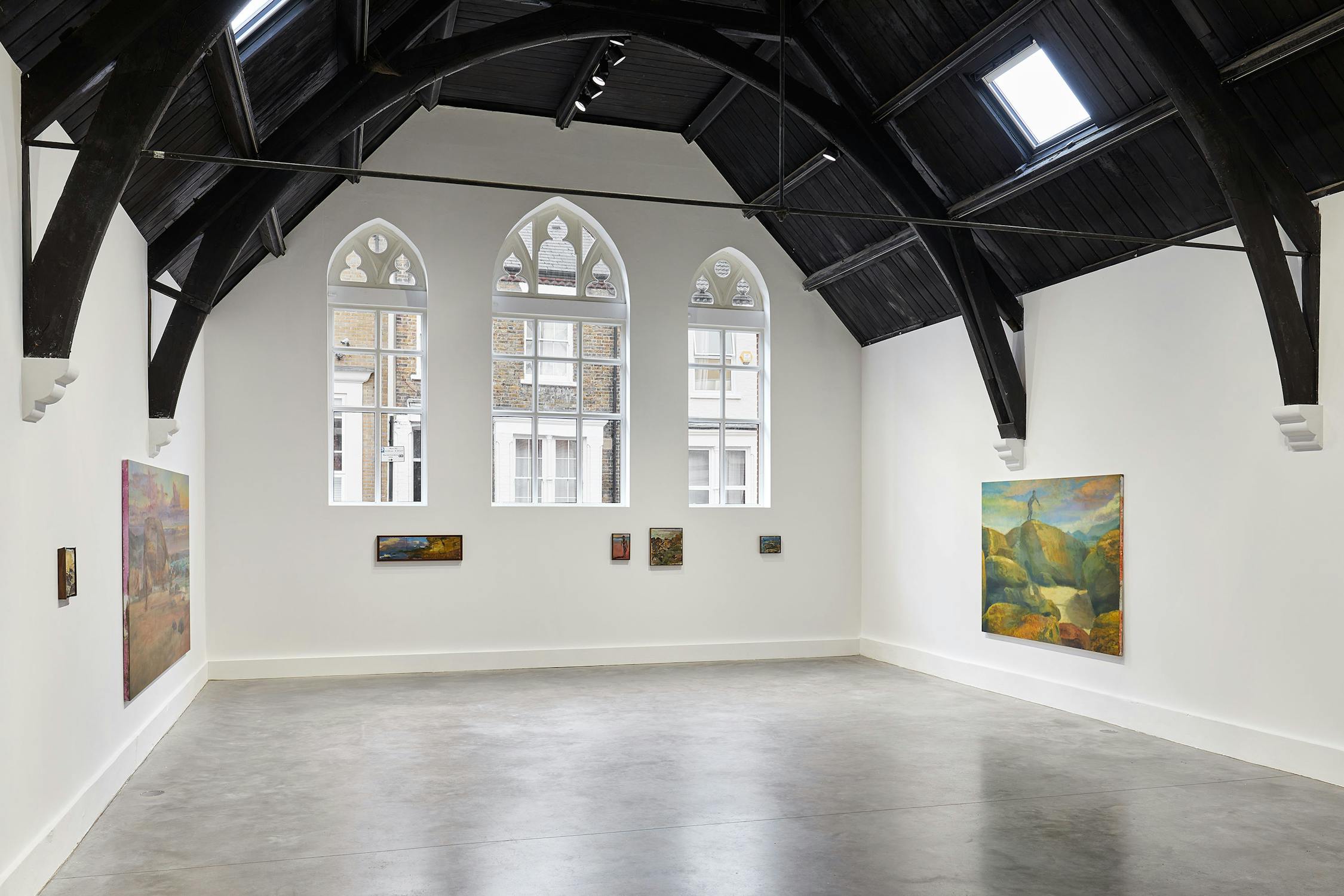 Art gallery with arched ceiling and large windows showcasing various paintings by Jake Grewal on white walls. The room is spacious and well-lit, featuring a mix of small and large artworks.