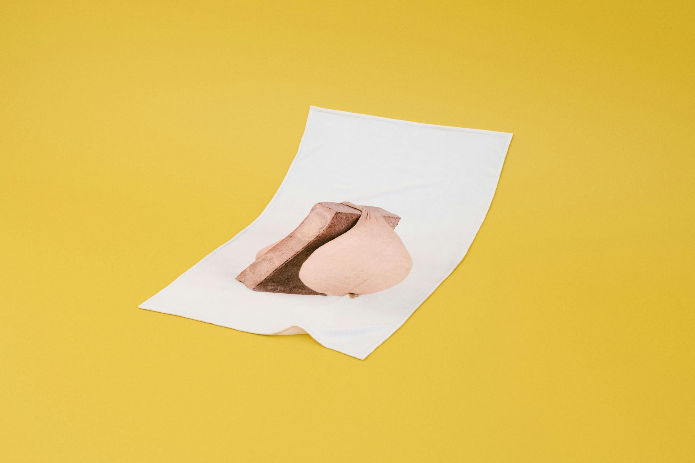 An image from Sarah Lucas' 'Tit Brick series' printed on a beach towel against a vibrant yellow background.