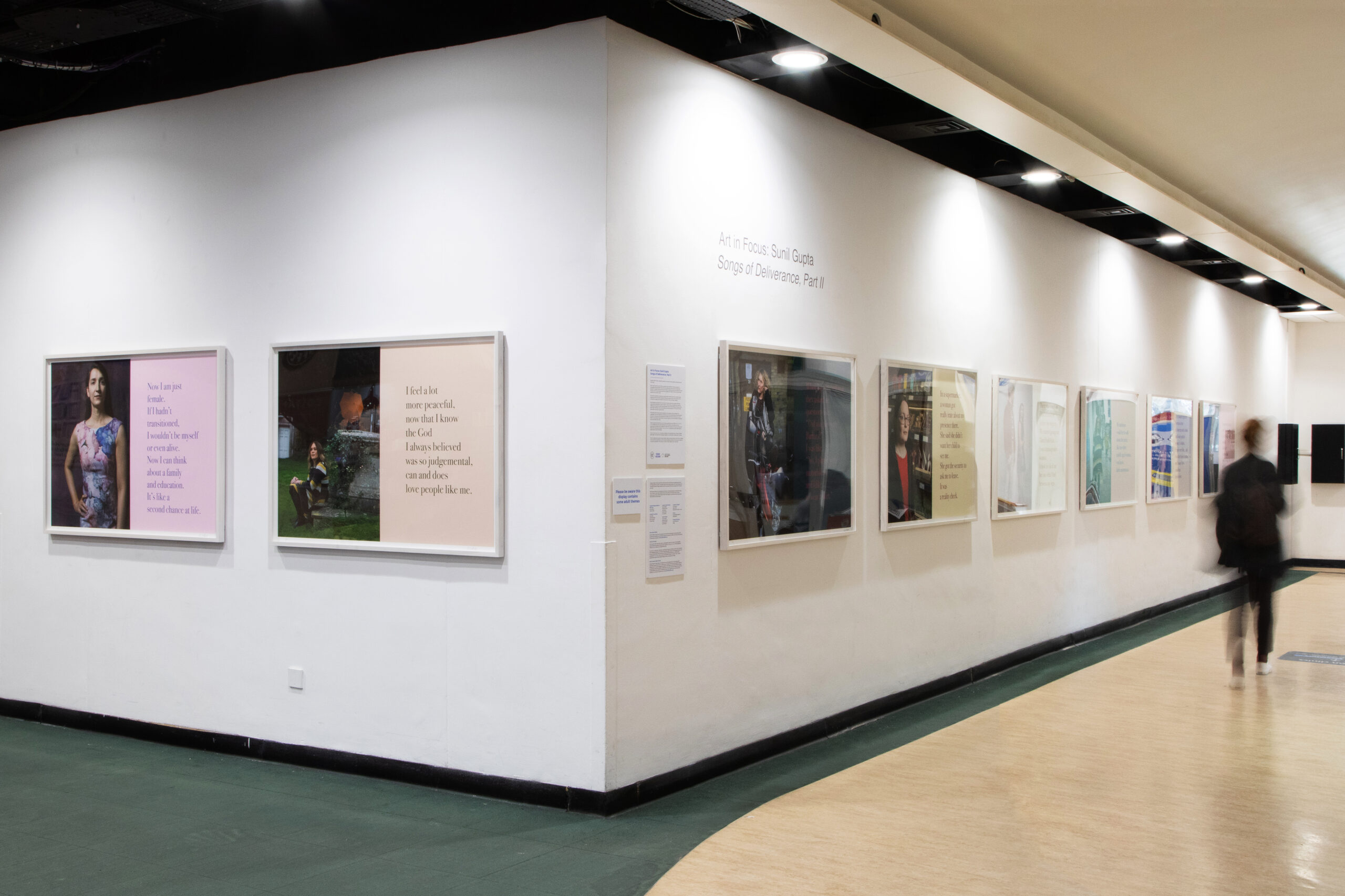 A well-lit art hospital hallway displaying a series of framed photographs and text on the walls. The floor is a mix of green tiles and light wood.