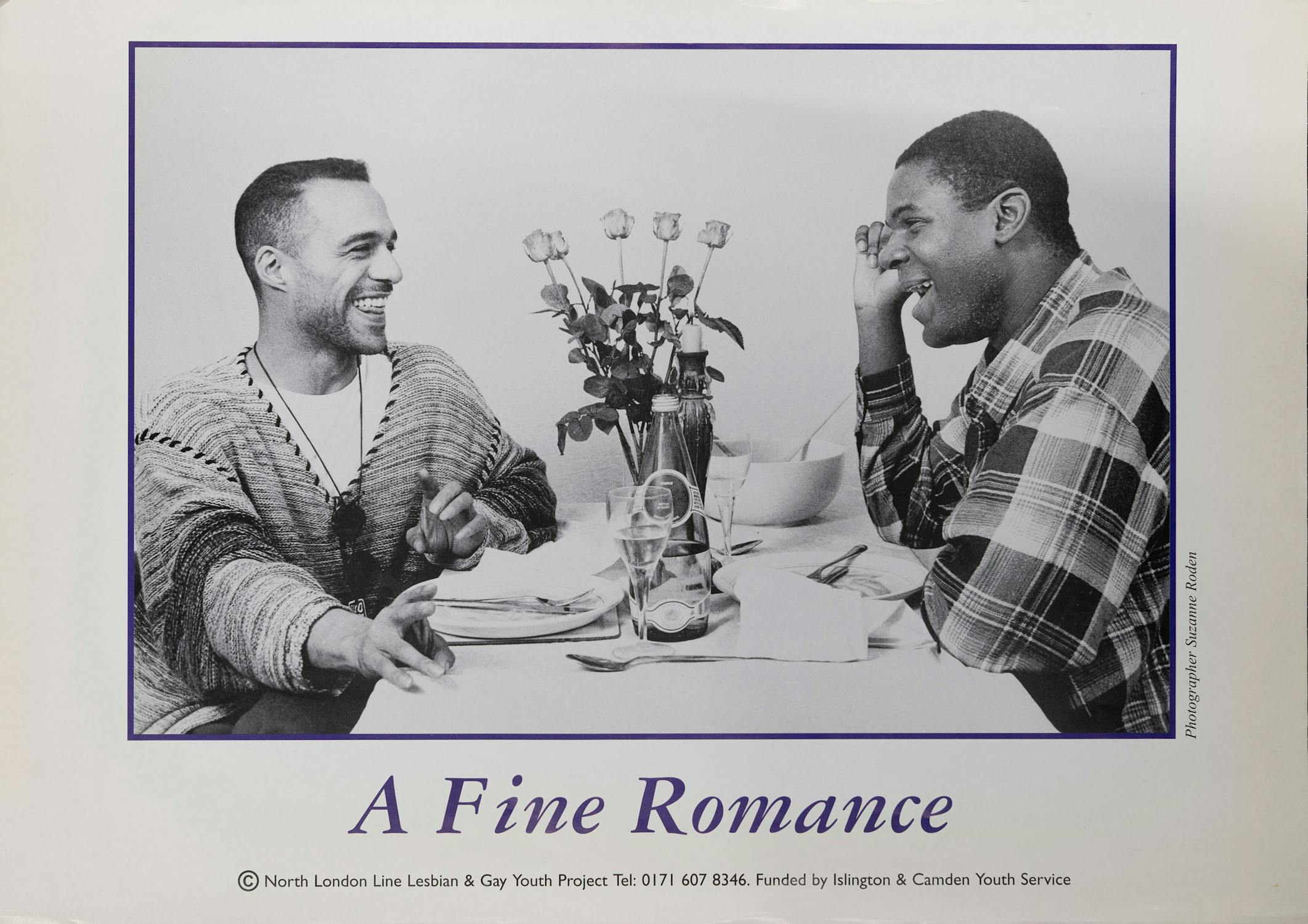 Two people sit across from each other at a dining table with white tablecloth. They are smiling and gazing at each other. A vase with roses is placed between them. Text at the bottom reads: "A Fine Romance.