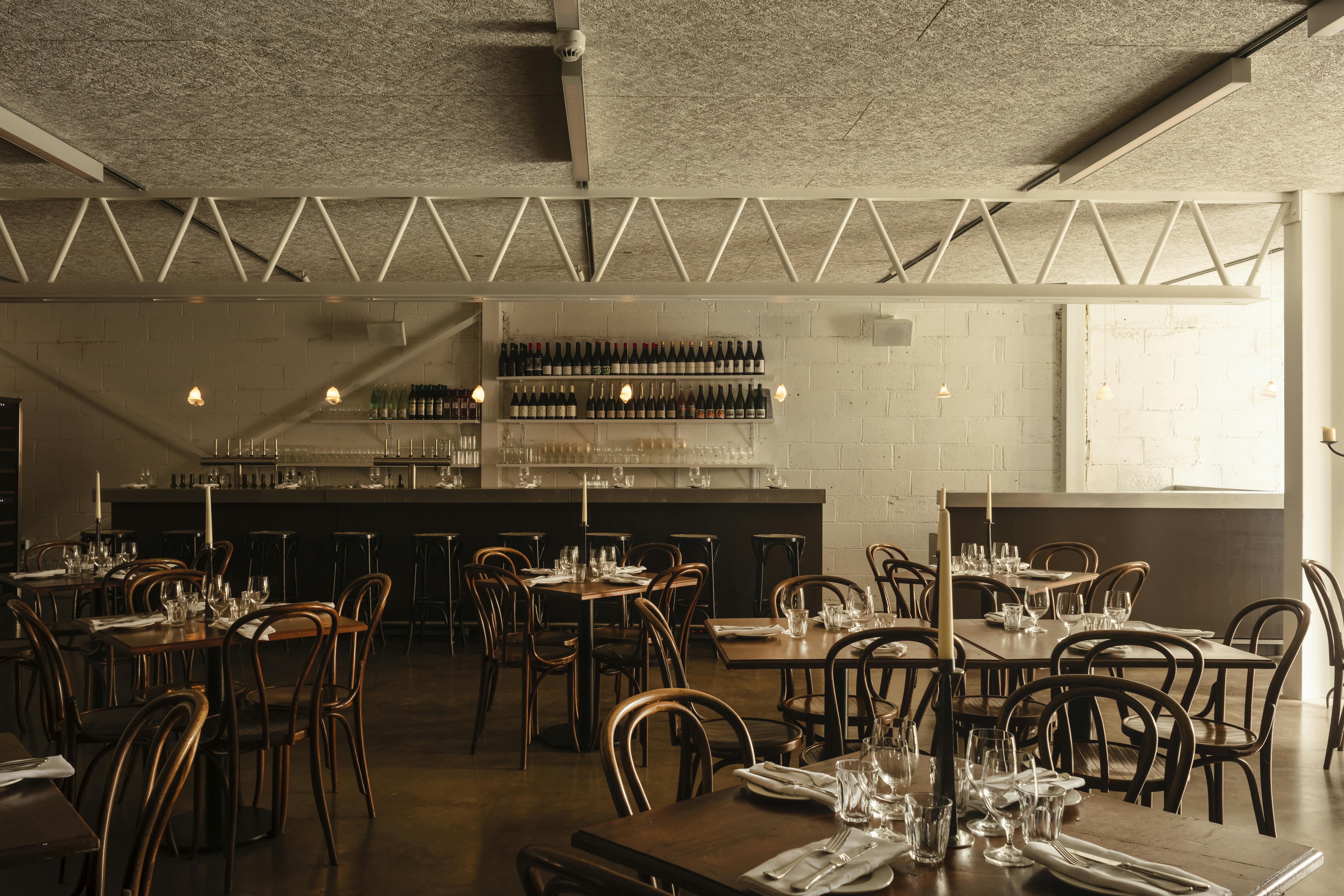 A photograph of Crispin at Studio Voltaire, a new restaurant. Set tables with candles, glasses and napkins are arranged in front of a bar area