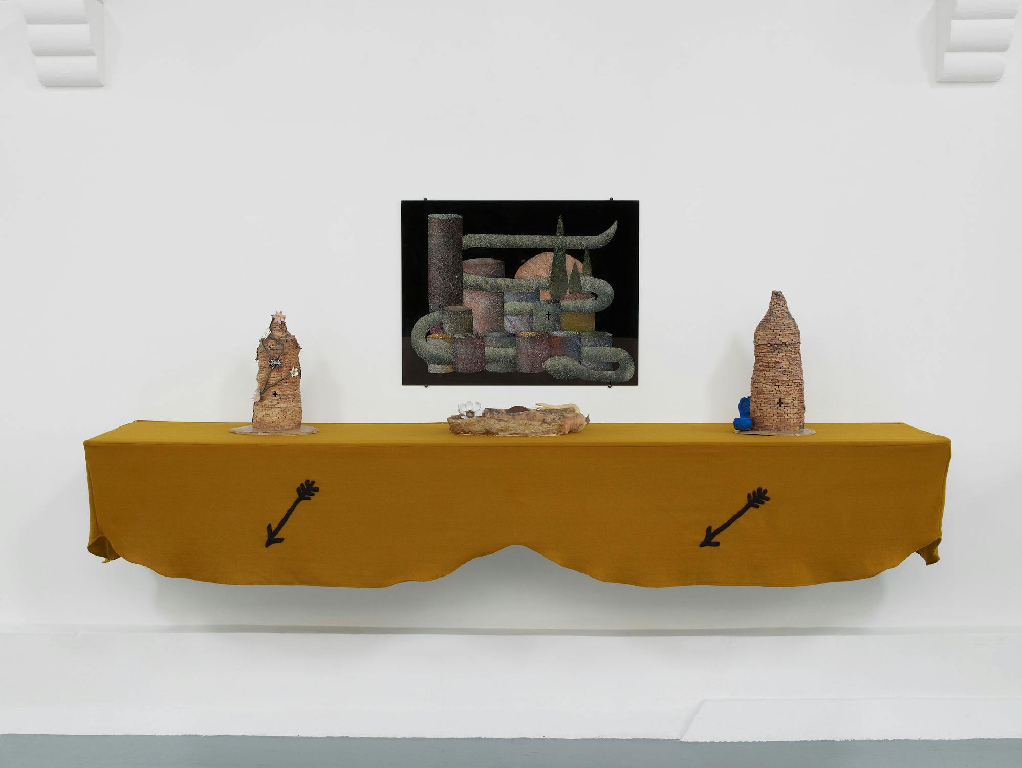 A view of an artwork installation comprising a wall-mounted shelf draped with mustard-coloured fabric. The display comprises three ceramic vessels. A wall-mounted artwork is displayed the shelf.