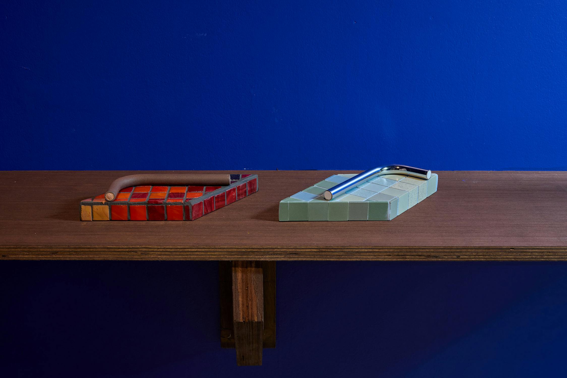 Two small tiled sculptures on a wooden shelf.
