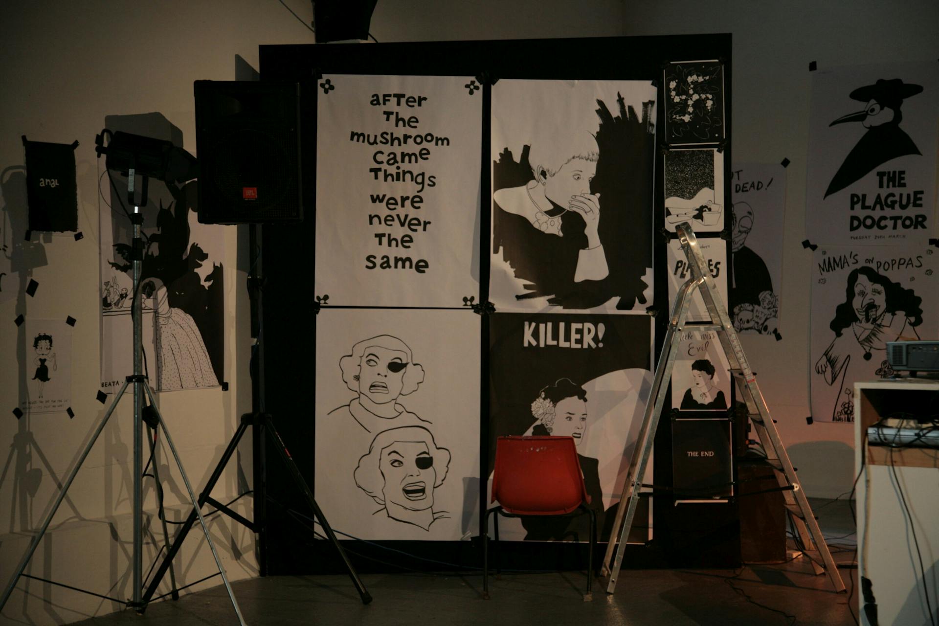a temporary wall with four black and white illustrated posters. a loudspeaker on a stand and a step ladder are seen in the foreground.