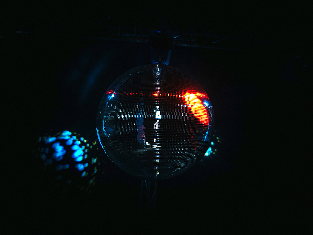 An image of a disco ball in a dark room, a bright light shines on the right hand side of the disco ball and its reflection is seen on the wall to the left.