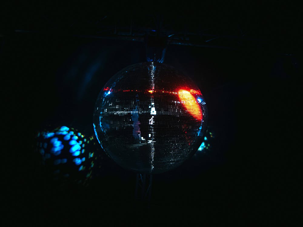An image of a disco ball in a dark room, a bright light shines on the right hand side of the disco ball and its reflection is seen on the wall to the left.