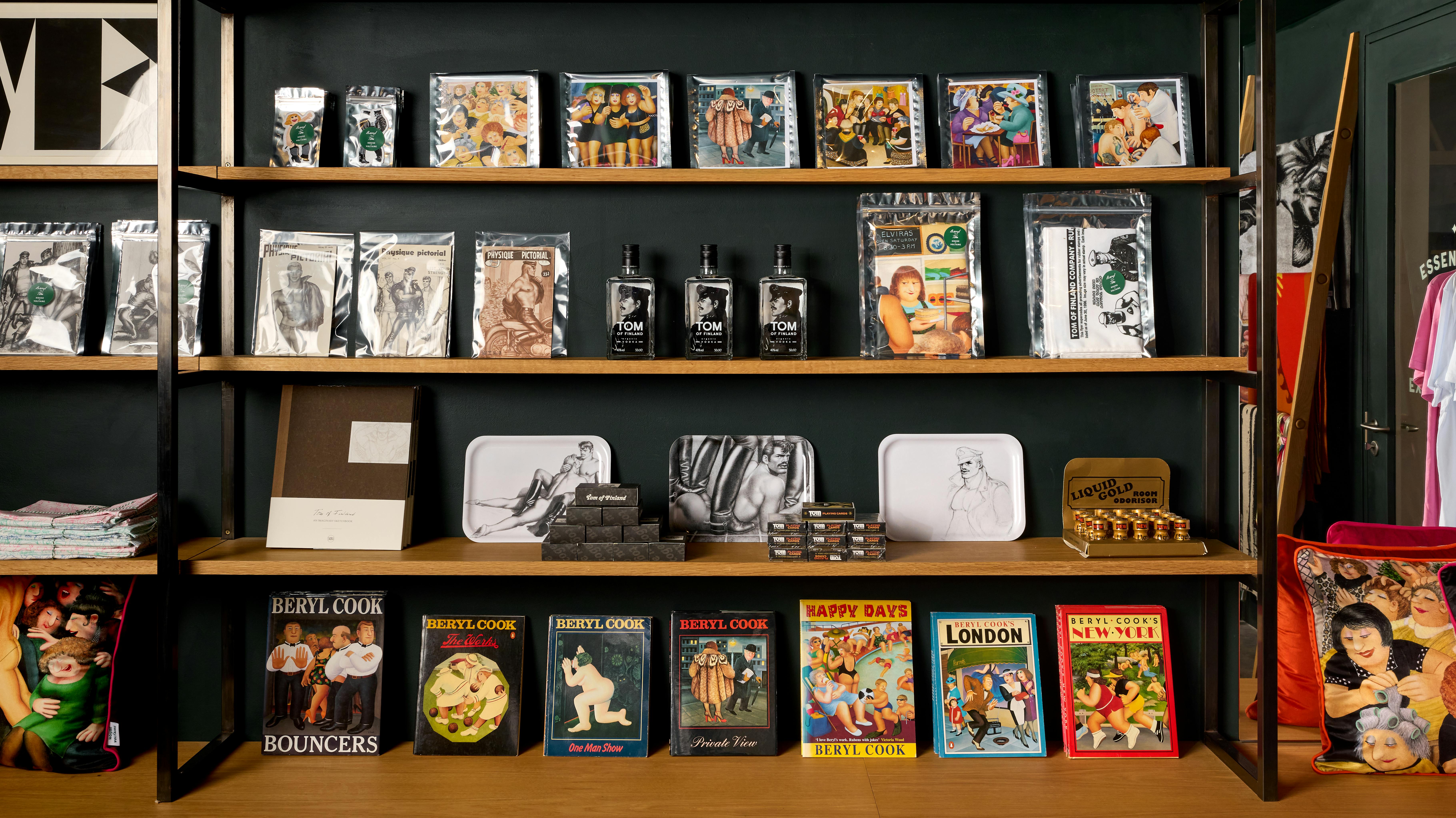 Shelves stacked with books, tea towels, greetings cards and other merchandise by Beryl Cook and Tom of Finland