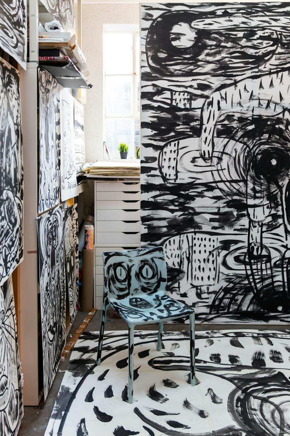 An artist's studio with walls, floor and a chair covered in large-scale black and white painted figures and patterns