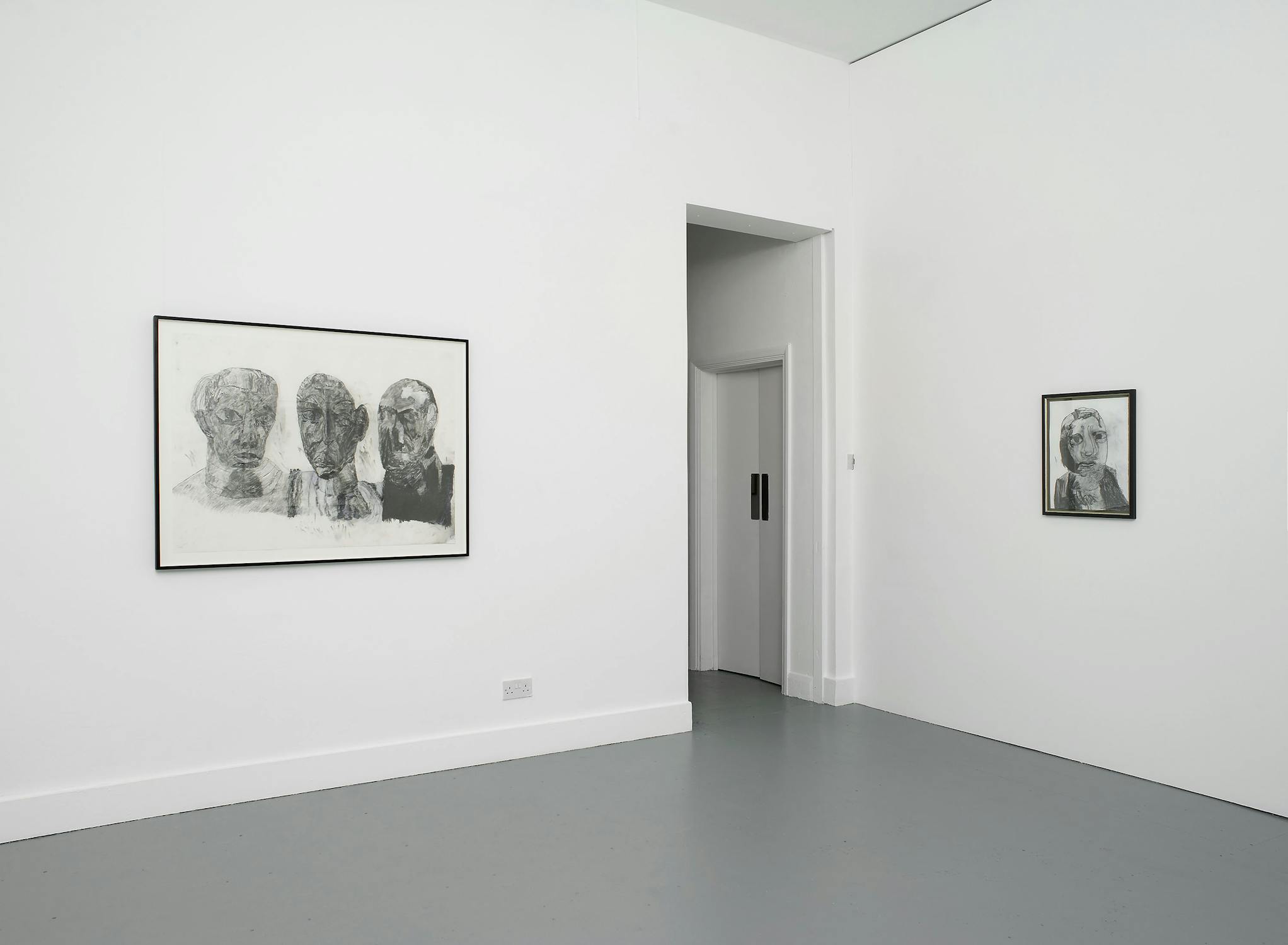 A pencil drawing of three figures with exaggerated features is hung beside a smaller similar portrait in the corner of a white-walled gallery