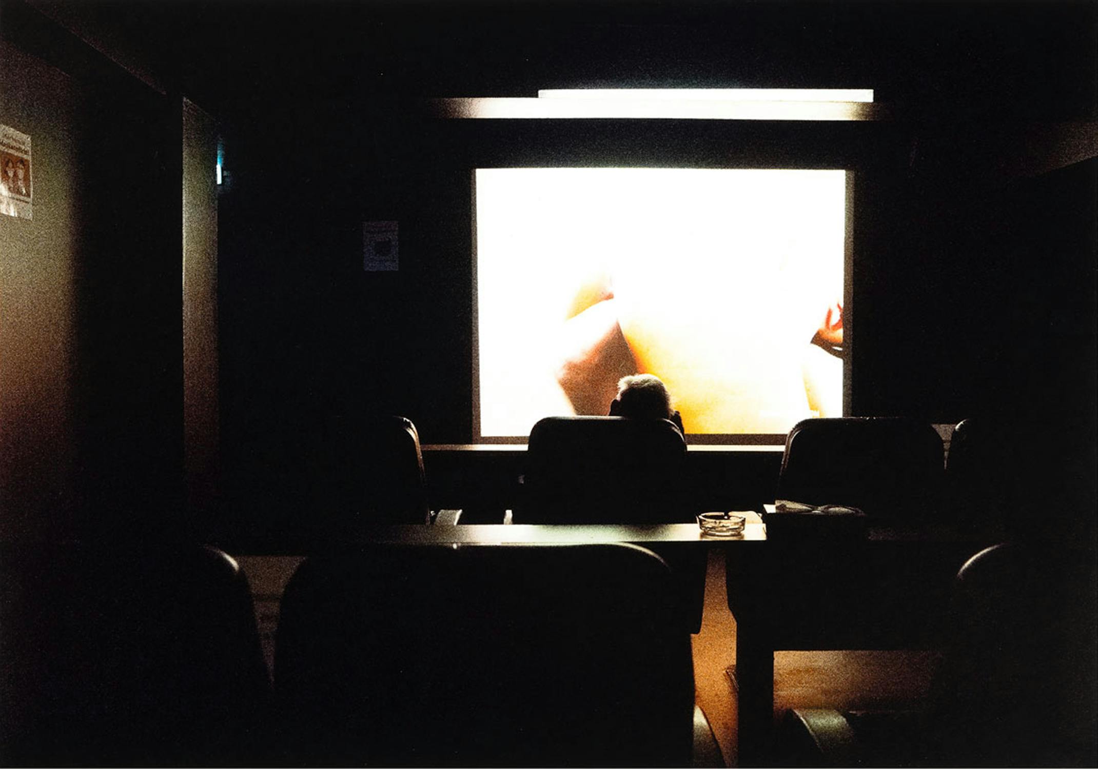 A gloomy high contrast photograph of a person facing away from the camera towards a bright window