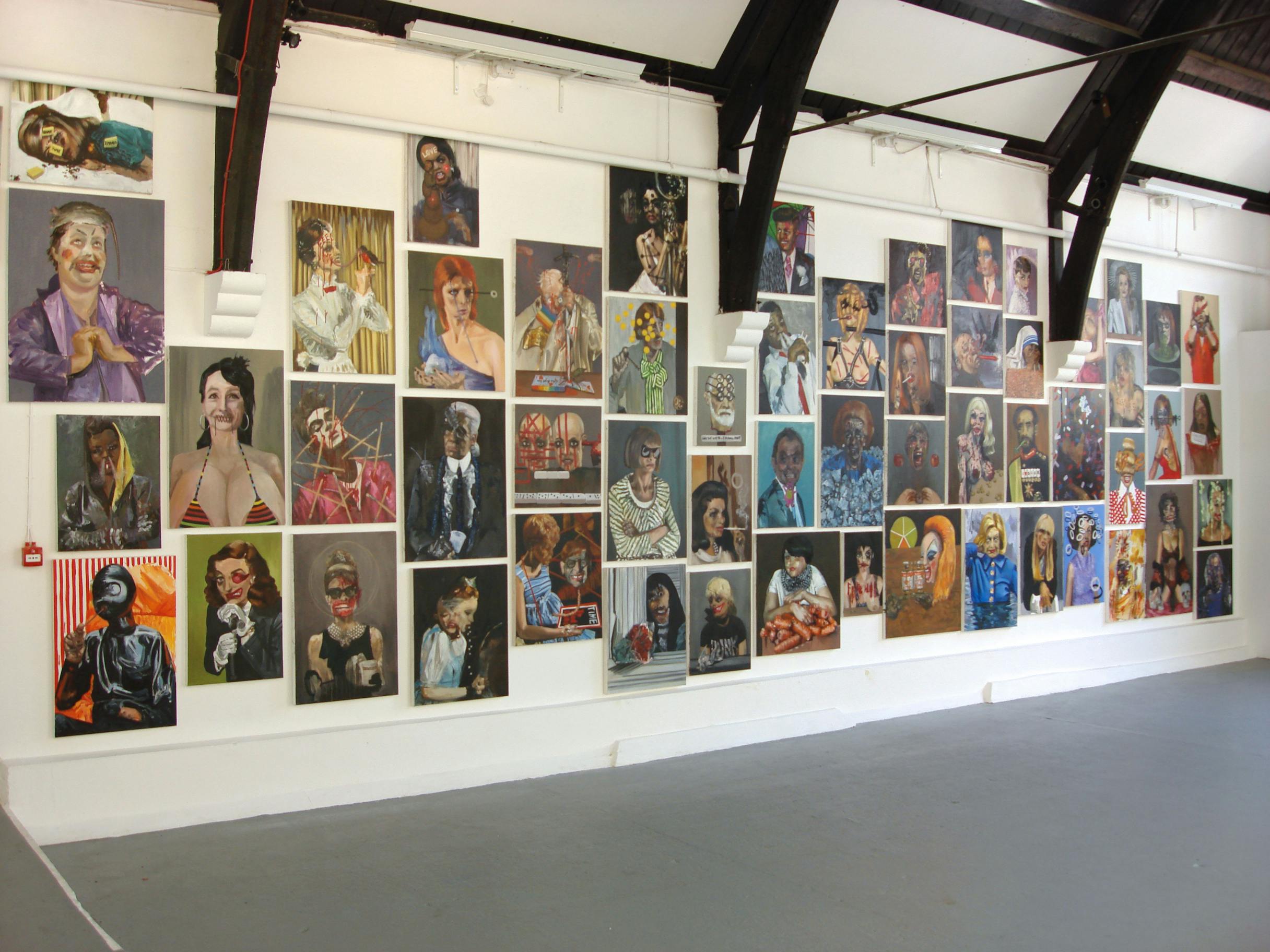 White gallery wall covered in satirical painted portraits, including many pop culture icons.