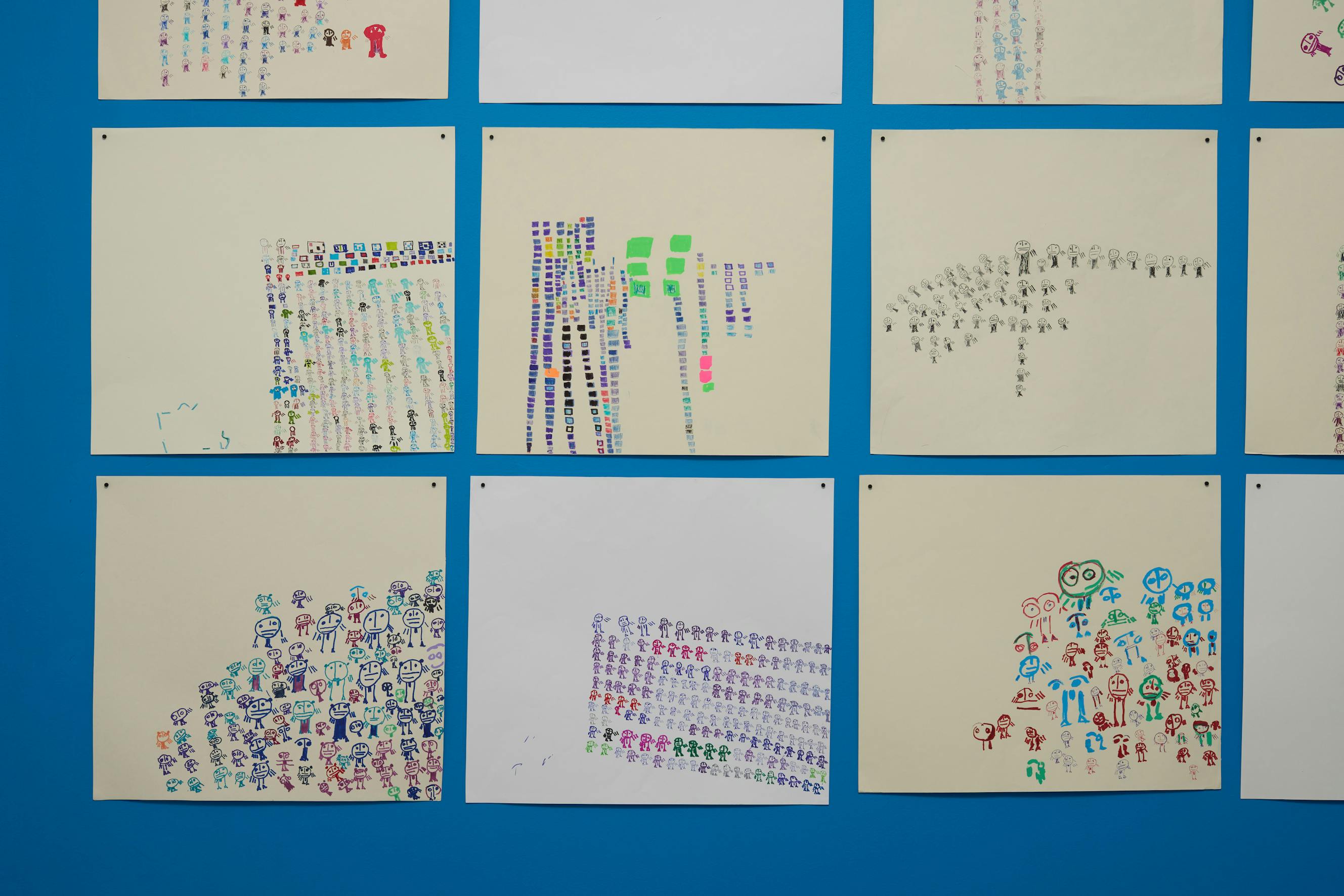 A collection of hand-drawn figures of various sizes and colours are displayed on a blue wall