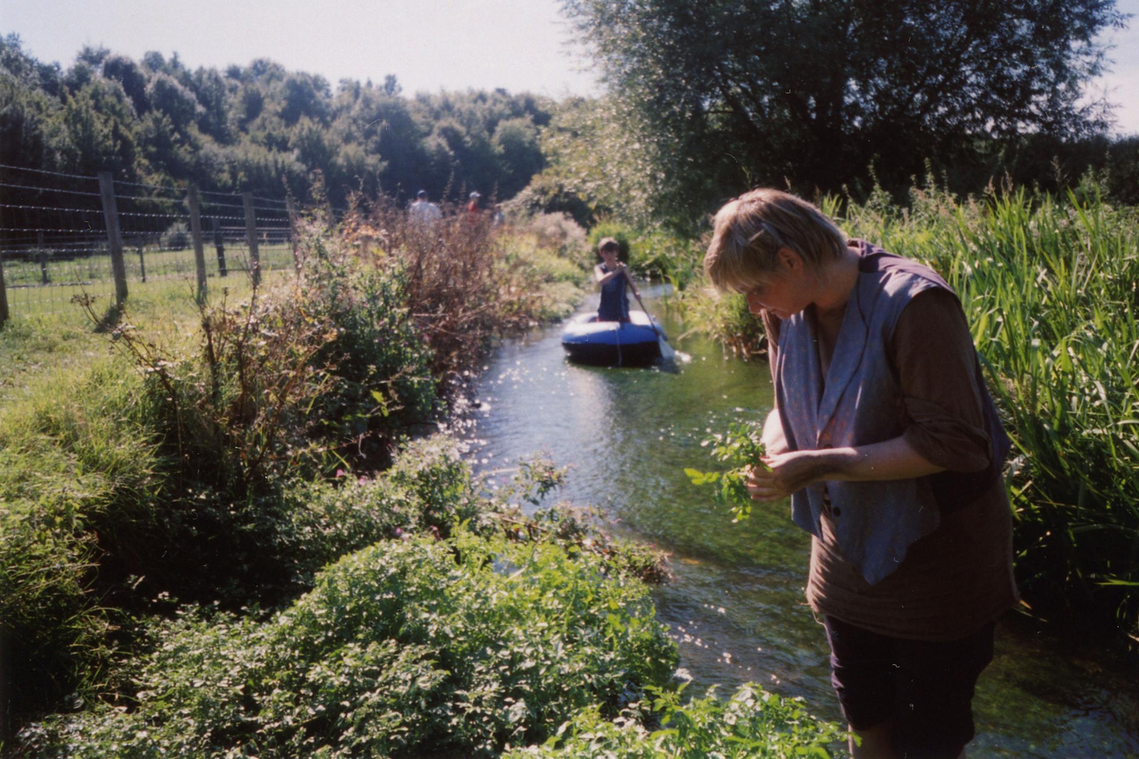 Film photograph of someone by a stream, someone else in a paddle boat