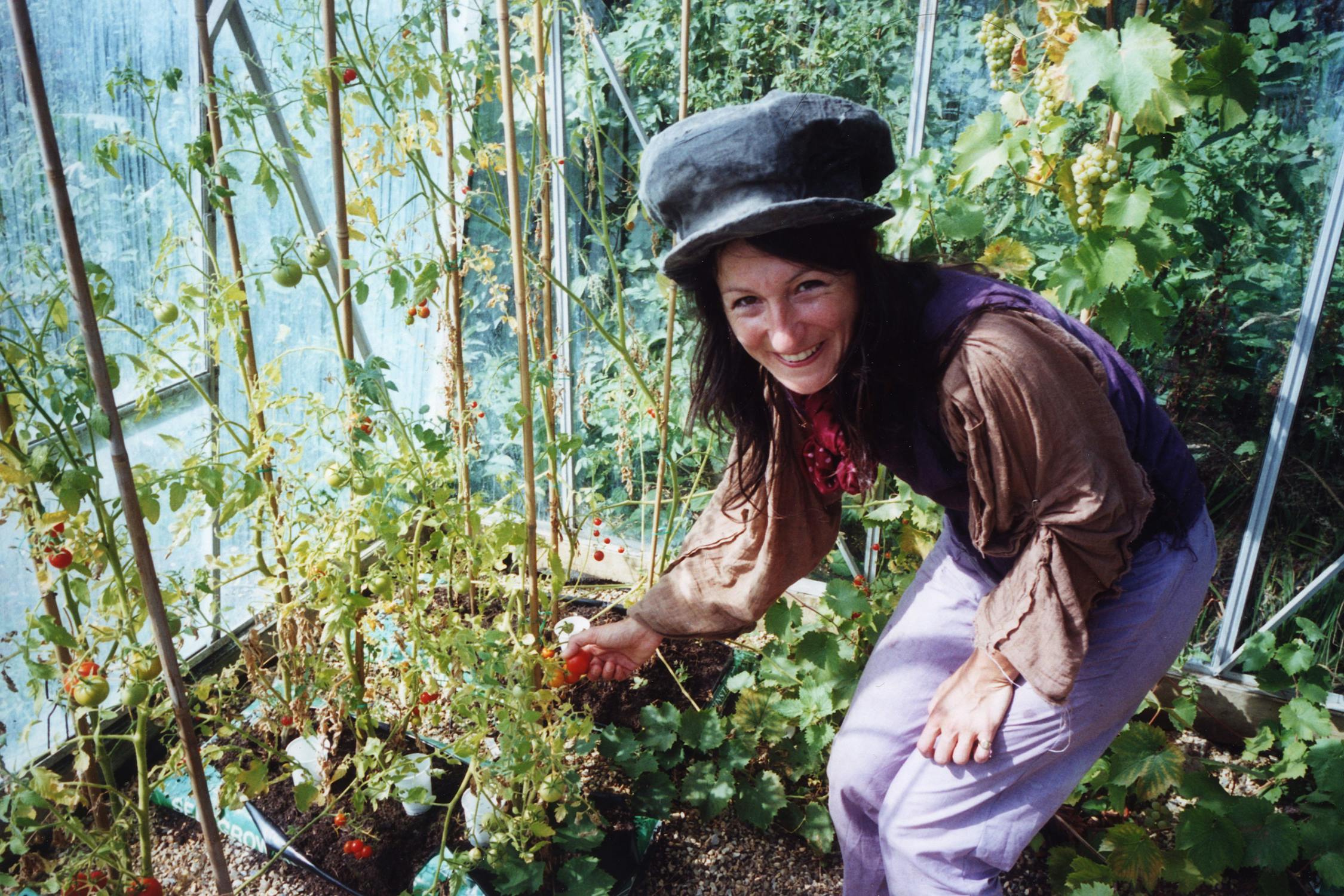 film photograph of someone smiling holding a tomato in a greenhouse