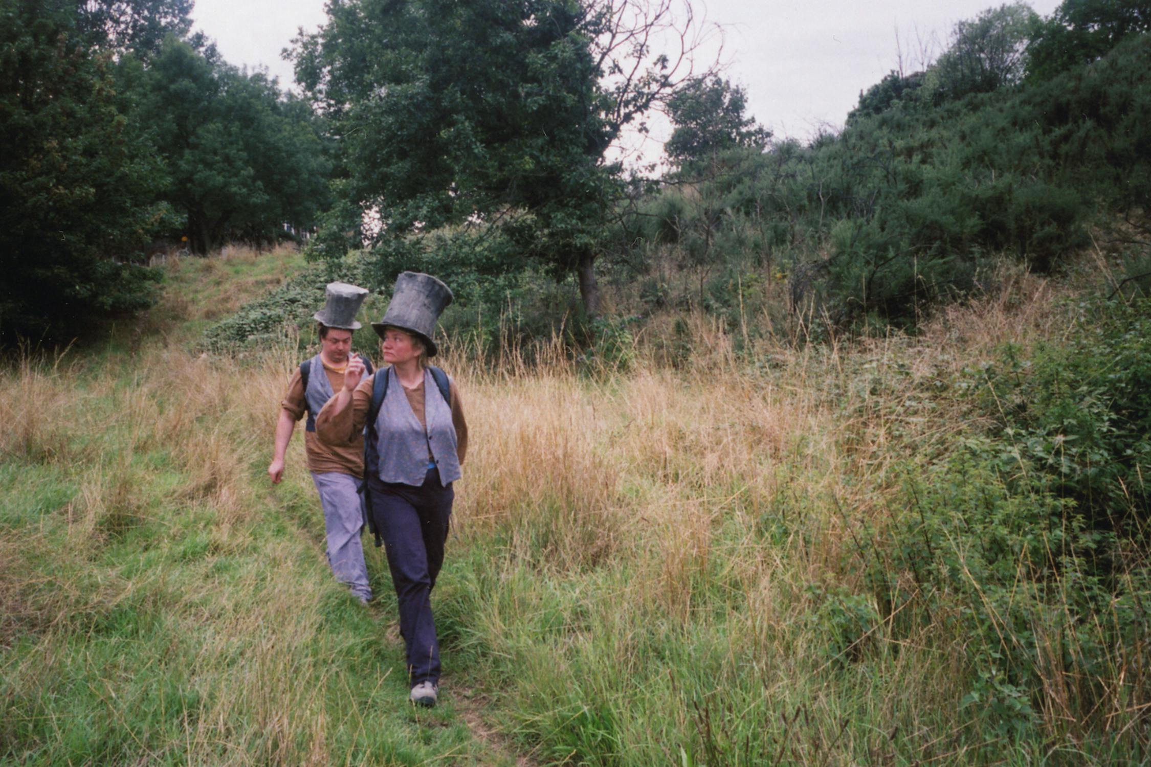 Film photograph of two people walking in a field wearing top hats