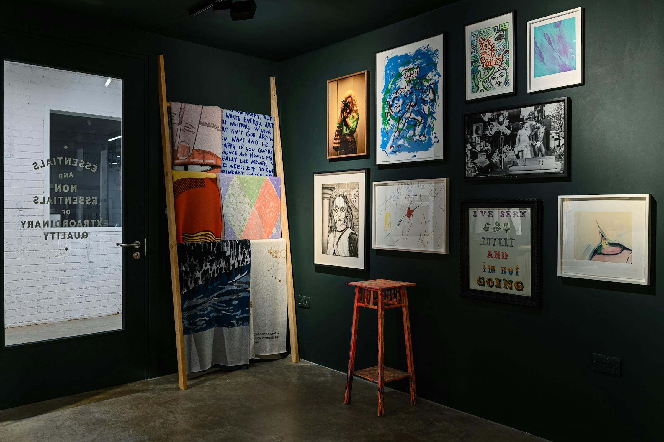 The interior of house of Voltaire's permanent store in Clapham: a room painted dark green, hung with colourful artworks and editions, with a rail of luxury knitted blankets