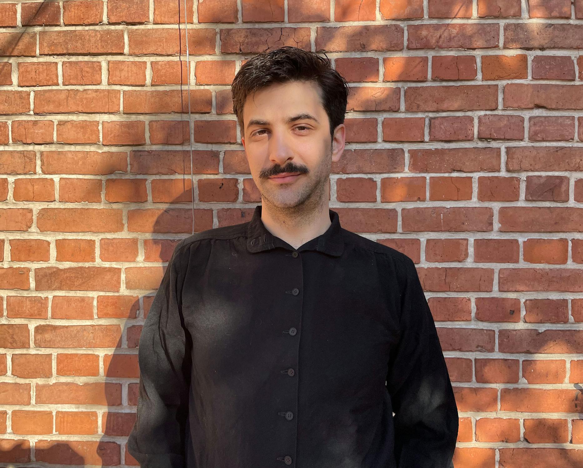 Artist Nicolás Said wearing a black shirt standing in front of a red brick wall