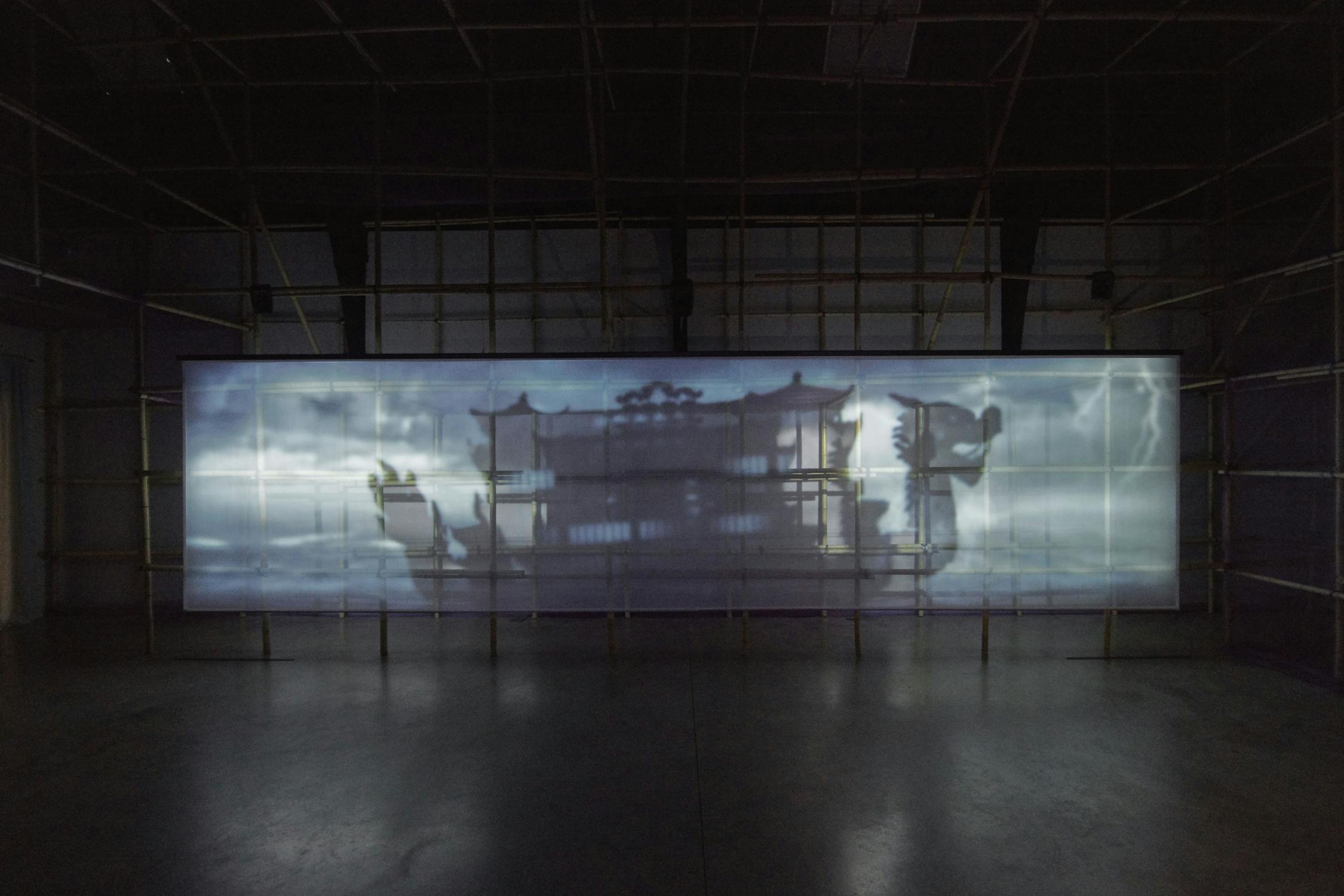 A dimly lit room features a large, semi-transparent screen with a shadowy projection of a floating dragon-shaped restaurant. The screen spans the width of the room, while the floor and surrounding walls are dark, adding to the mysterious ambiance.