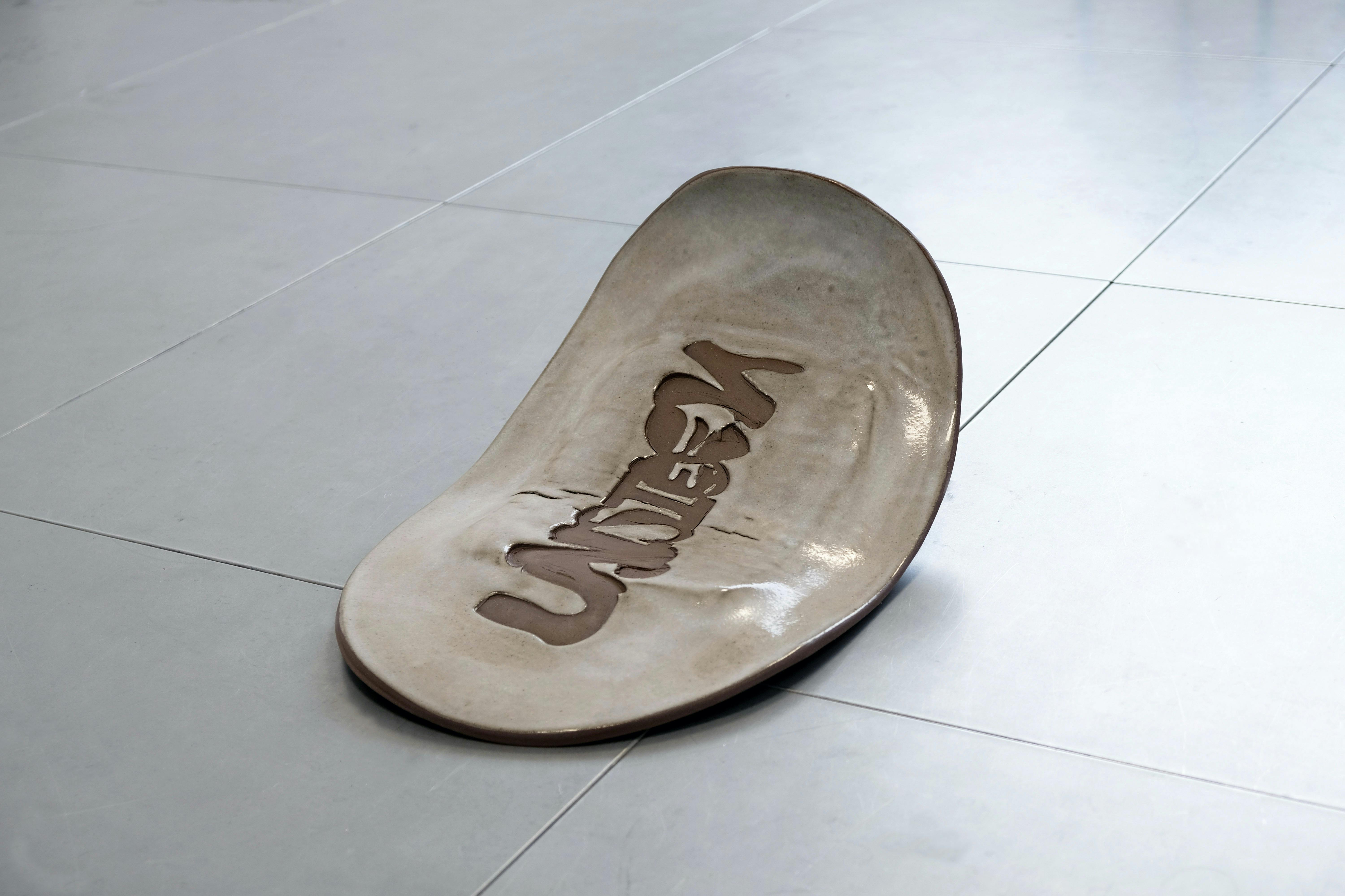 A large, curved, white ceramic sculpture rests on a tiled floor. The sculpture features the world 'UNSEEN', creating a unique artistic effect.