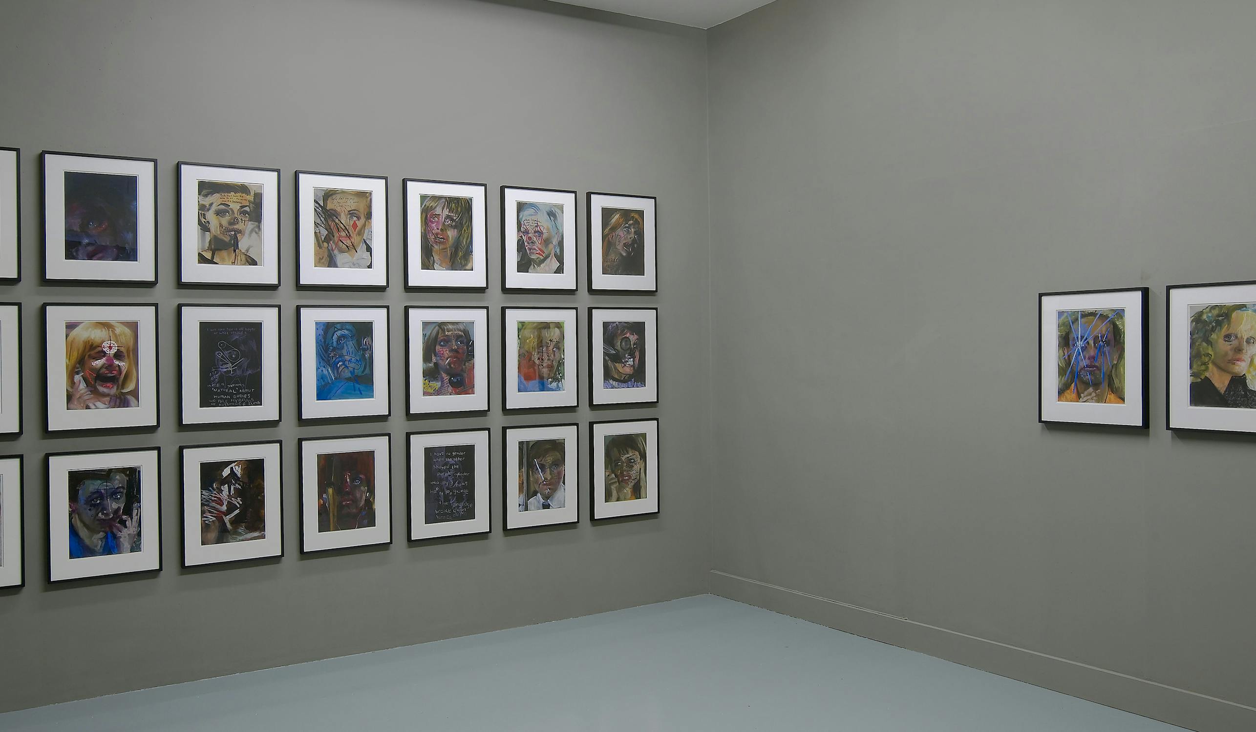 A gallery wall displaying a series of framed abstract portraits. The art features vibrant colors and expressive brushwork. Most frames are arranged in a grid on a gray wall, with a smaller group of pictures on the adjacent wall.