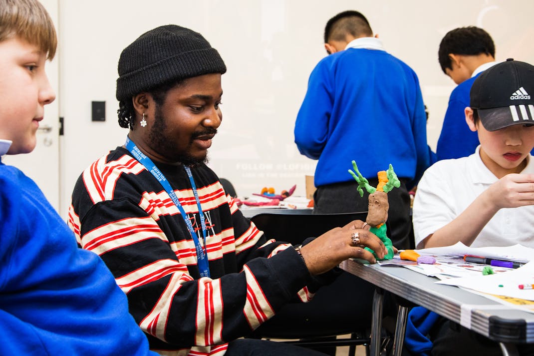 artist Djofray Makumbu  creates a green and orange plasticine figure with a school group
