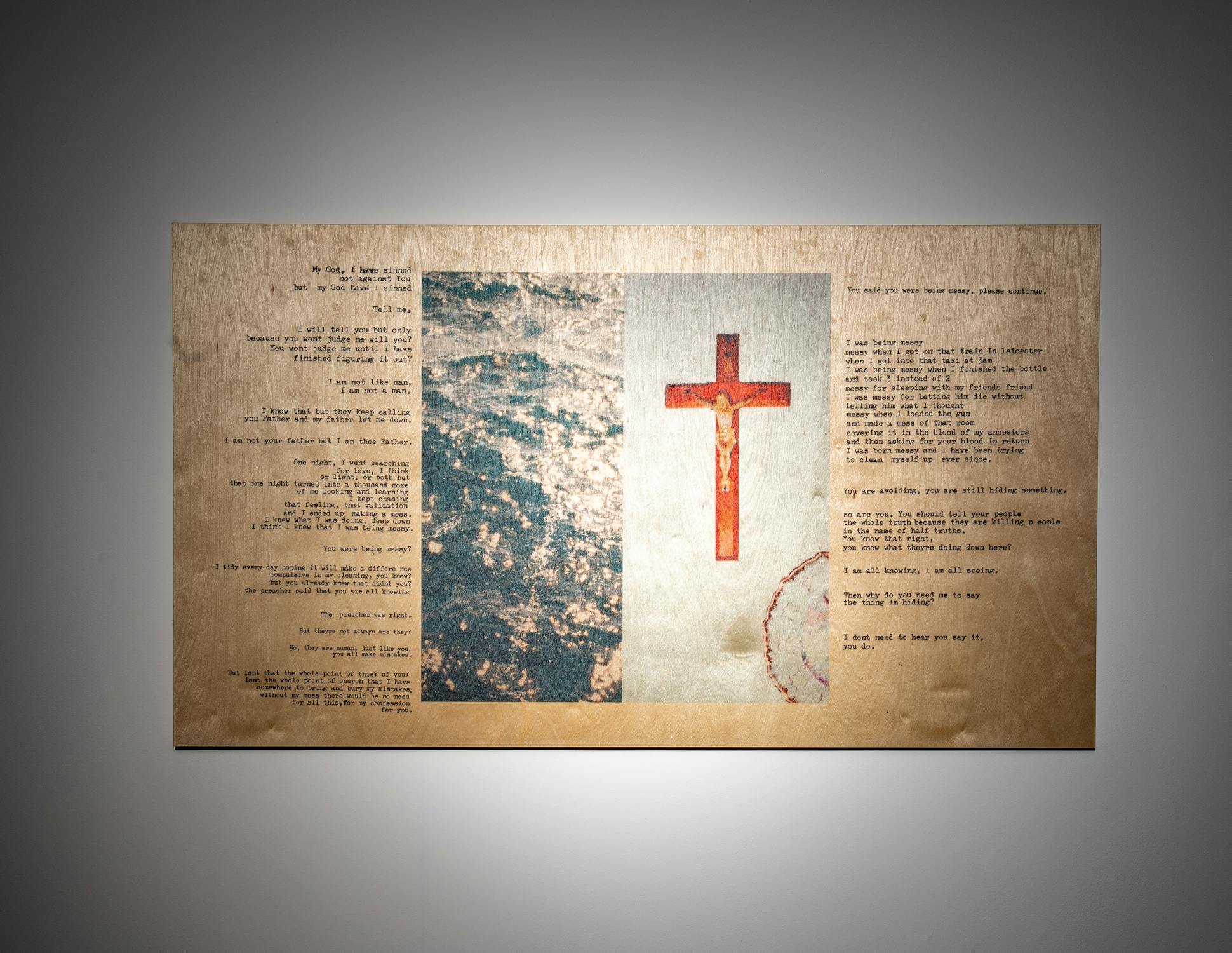A rectangular artwork mounted on a wall features typewritten text on both sides, an image of a wooden crucifix in the centre right, and a textured blue and white abstract image in the centre left.