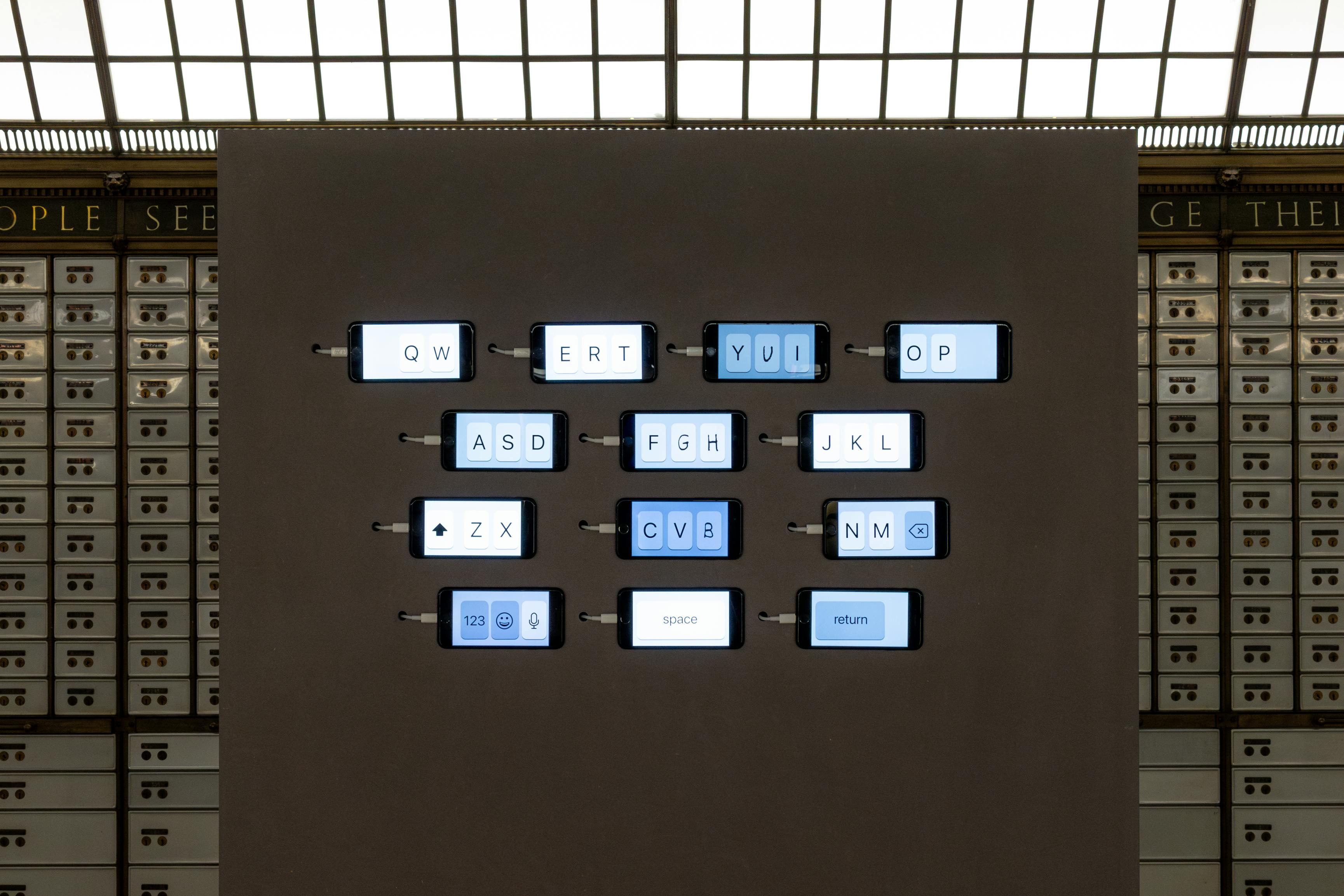 A display features large illuminated keys arranged like a QWERTY keyboard embedded in a dark panel, with each key backlit and labelled. Rows of small drawers line the background wall.
