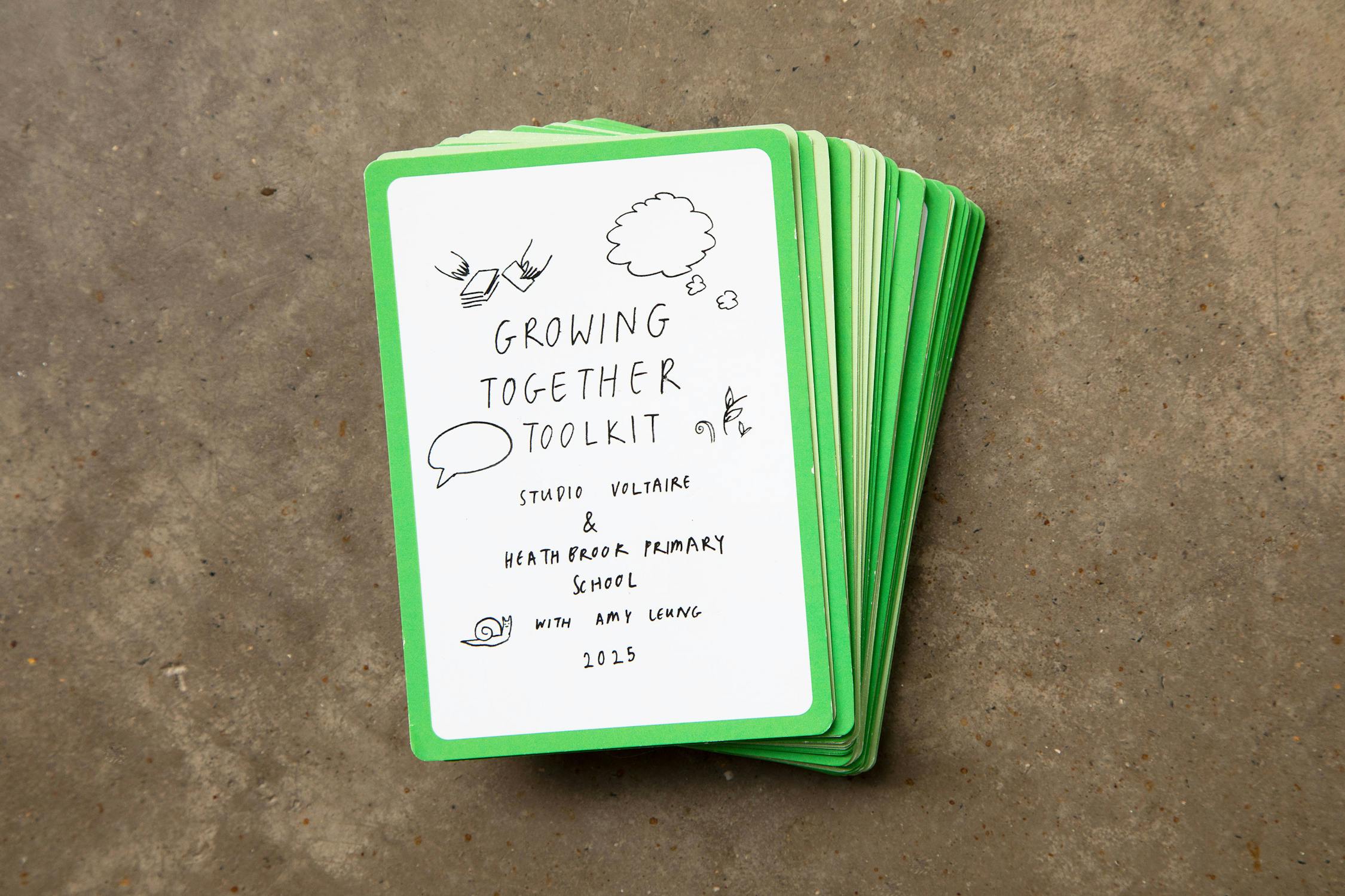A stack of green-edged cards on a concrete surface. The top card reads "Growing Together Toolkit" with hand-drawn illustrations and credits Studio Voltaire, Heathbrook Primary School, and Amy Leung, dated 2025.