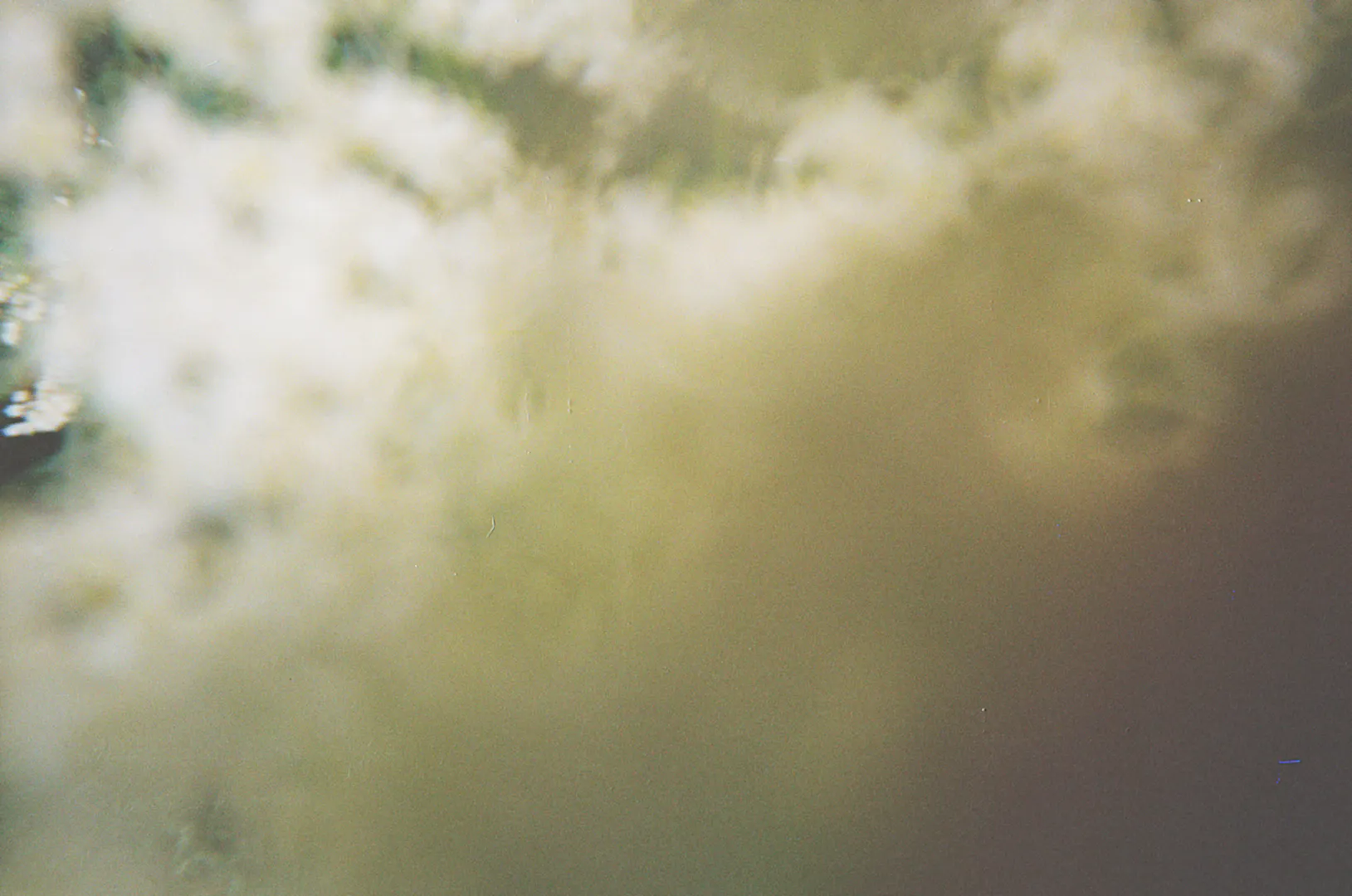 An abstract, blurry image with soft, cloudy white and beige areas blending together, suggesting an out-of-focus shot. The light diffuses across the frame, creating a dreamy, indistinct atmosphere with no clear shapes or objects visible.