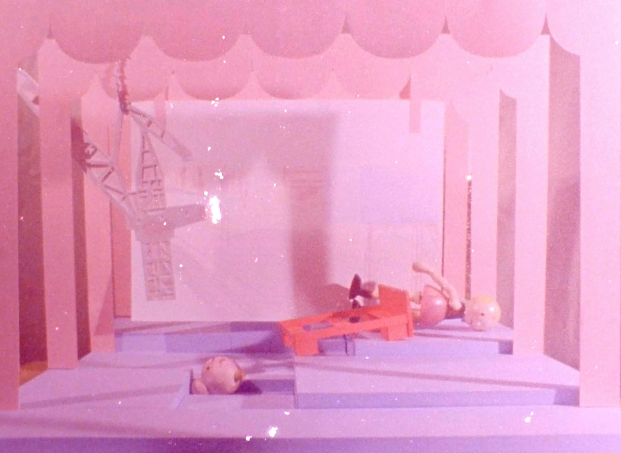 A pastel pink and purple diorama features a cloud-like top border, geometric shapes as floors and walls, a red bench, and three small, round dolls positioned at odd angles