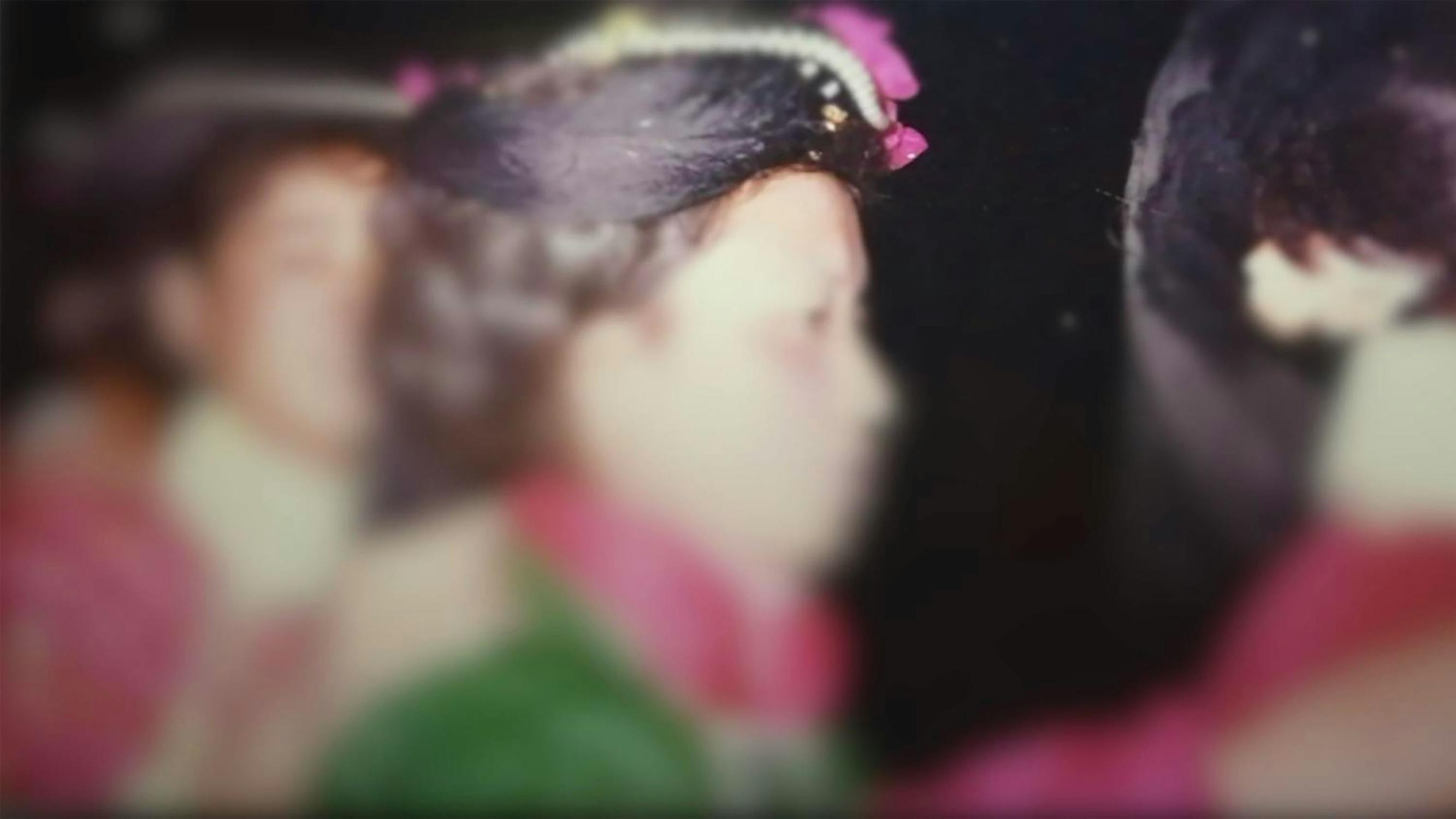 A blurry film still shows a woman in profile, wearing traditional attire with colourful fabric and a decorated headdress. Another figure is visible in the background, also dressed similarly.
