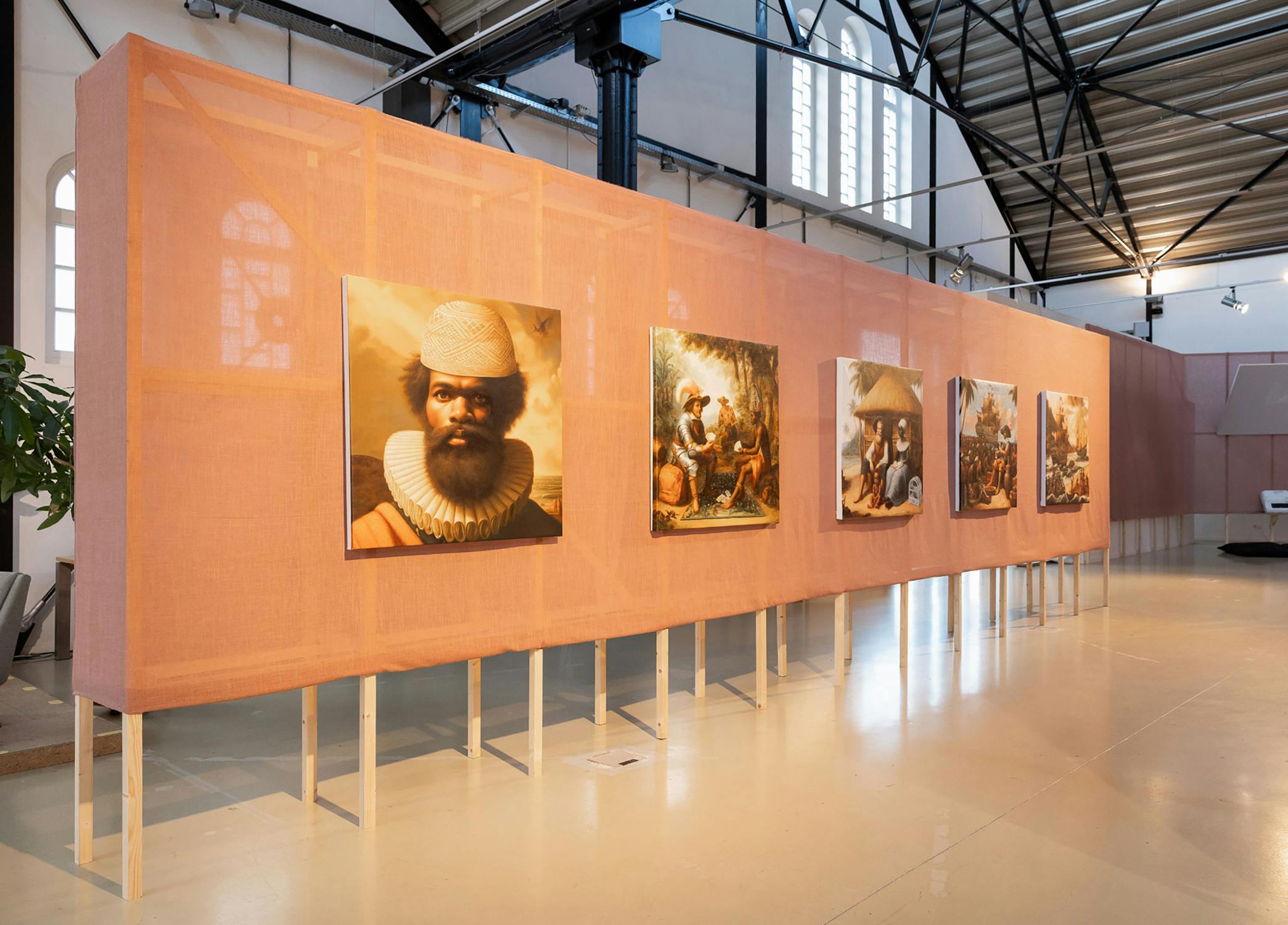 A museum exhibit features five historical paintings mounted on a long, peach-toned fabric-covered wall. The paintings depict scenes and portraits that allude to colonial history. The gallery has high ceilings, large windows, and exposed beams.