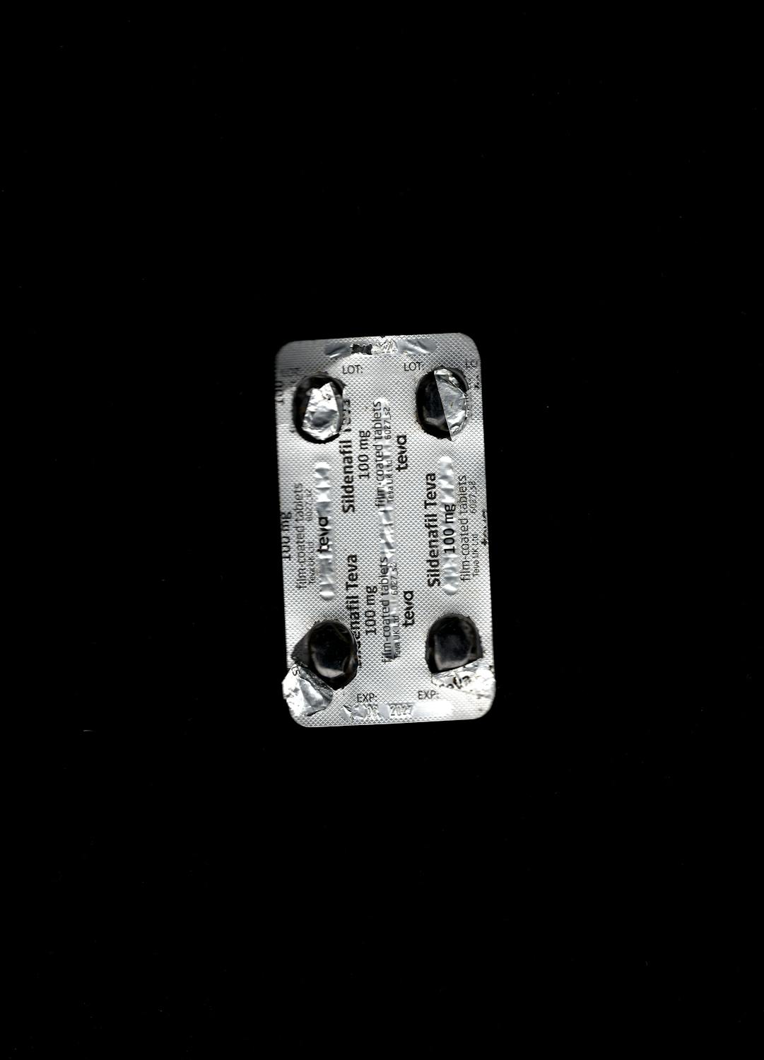 A silver blister pack with four empty pill pockets sits on a black background. The pack is labelled "Sildenafil Tablets 100 mg" in black text, indicating it originally contained medication. The foil is torn where the pills were removed.