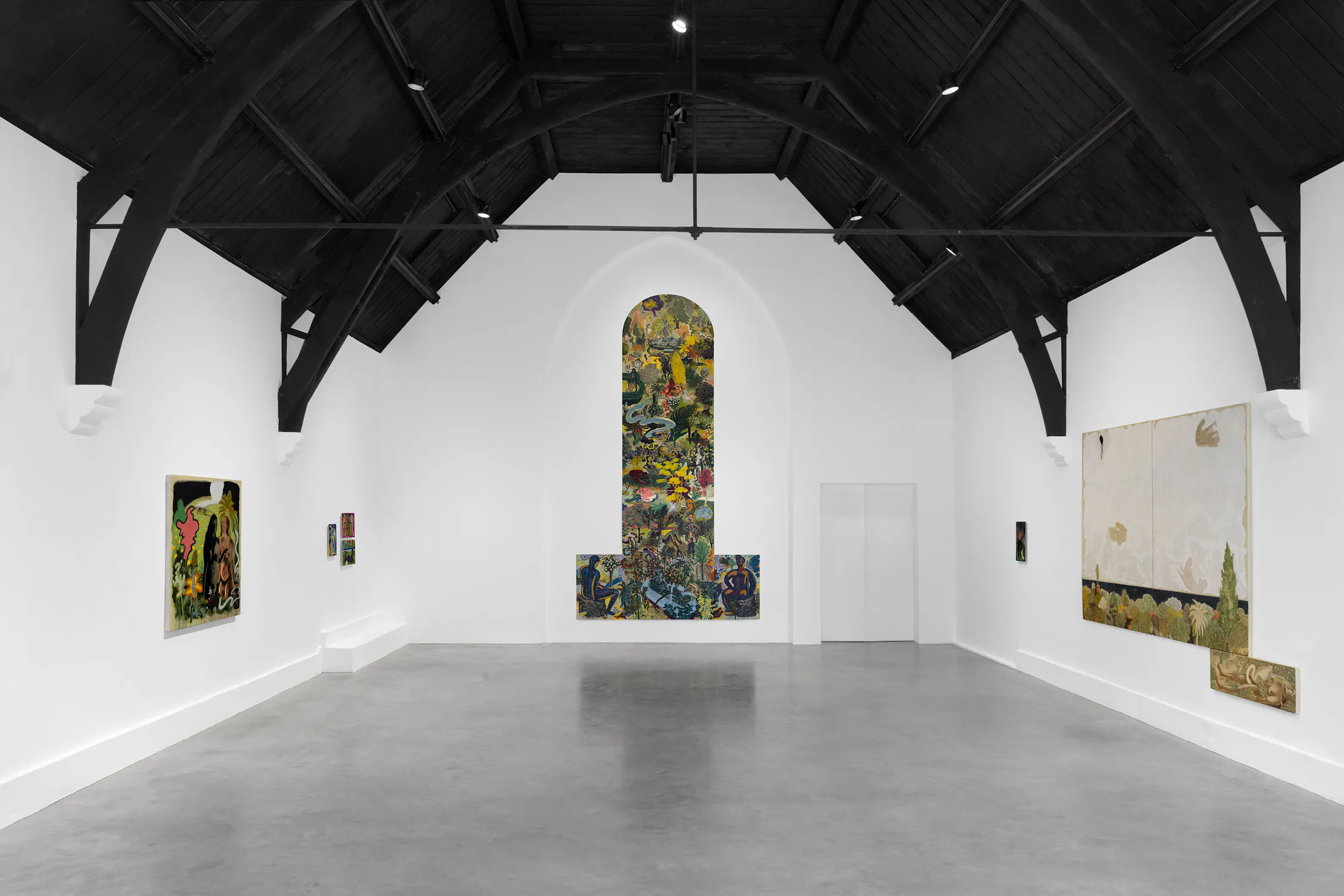 A modern art gallery with white walls, a high dark vaulted ceiling, and a grey floor. Large, colourful abstract paintings are displayed on the walls, including a tall central artwork framed by an arched recess at the end of the room.