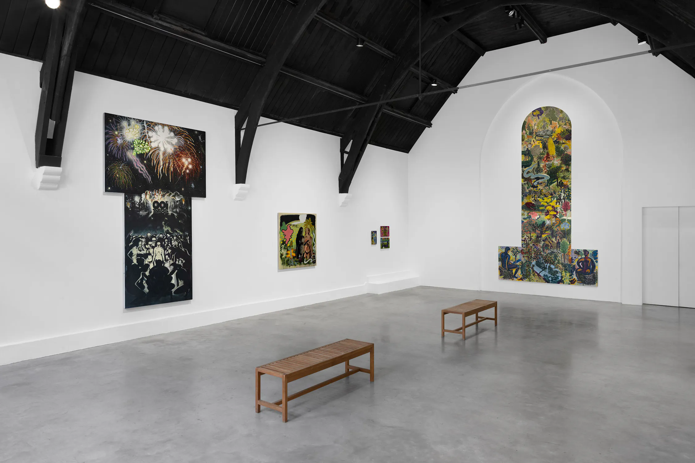 A modern art gallery with white walls, high dark ceilings, and arched beams displays colourful abstract paintings by T. Venkanna. Two wooden benches sit on the grey floor. The largest artwork is set in an arched niche; others hang on flat walls. The space feels bright and spacious.