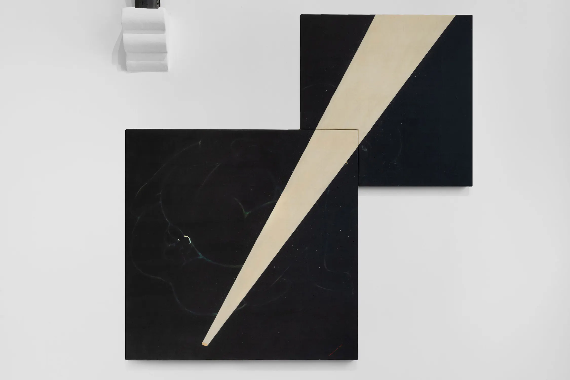 Two overlapping black square canvases hang on a white wall. A bold, cream-coloured diagonal beam cuts across both canvases from lower left to upper right, creating a striking contrast against the dark background.