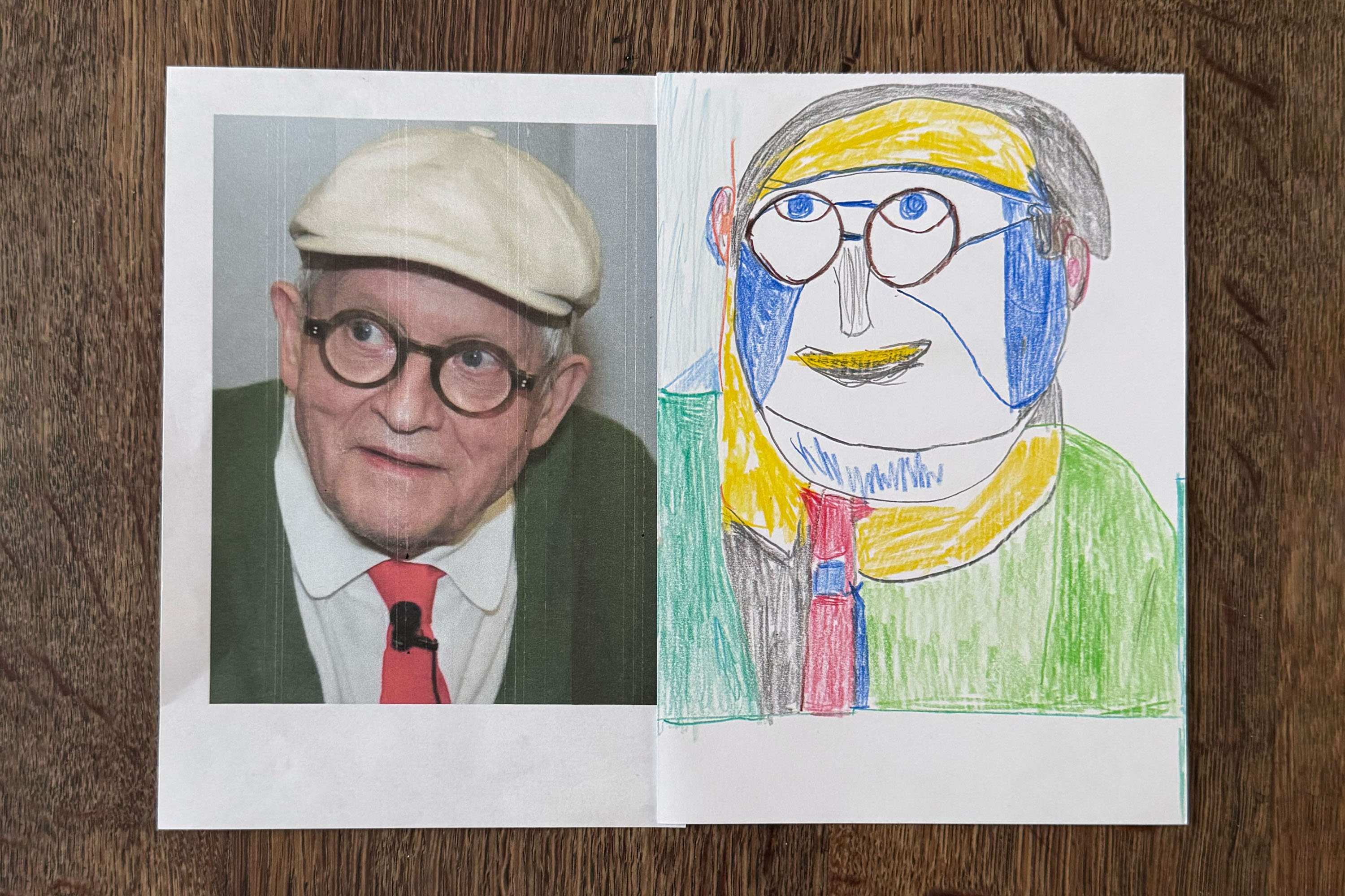 A photo of artist David Hockney, with glasses, a white cap, red tie, and green jumper, is on the left. On the right is a colourful, abstract crayon drawing by Christine Hazell of the same man, mimicking his features in a playful, childlike style. Both are on white paper.
